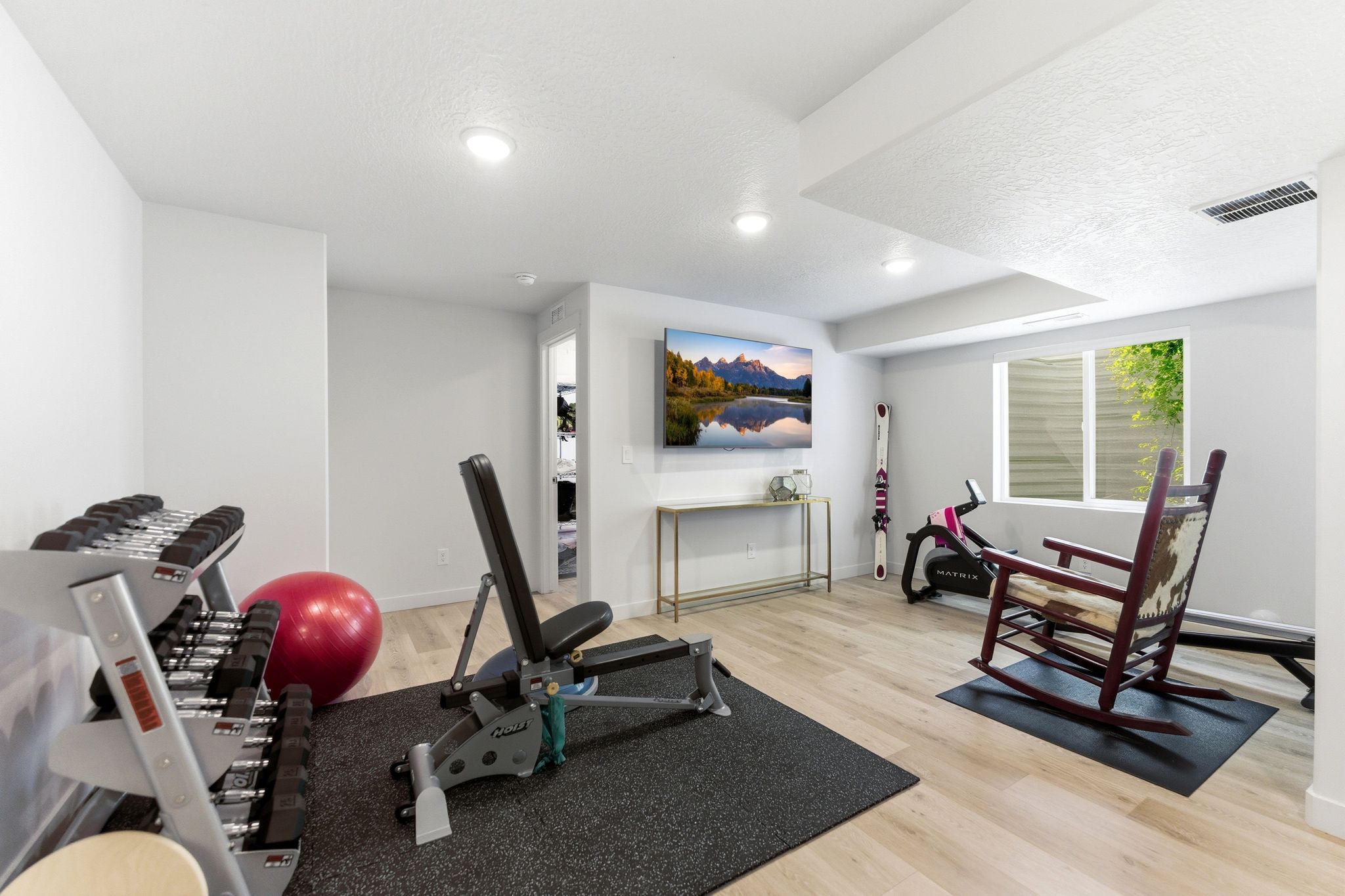 Versatile finished basement space with recessed lighting, light wood-finish flooring, and a large egress window