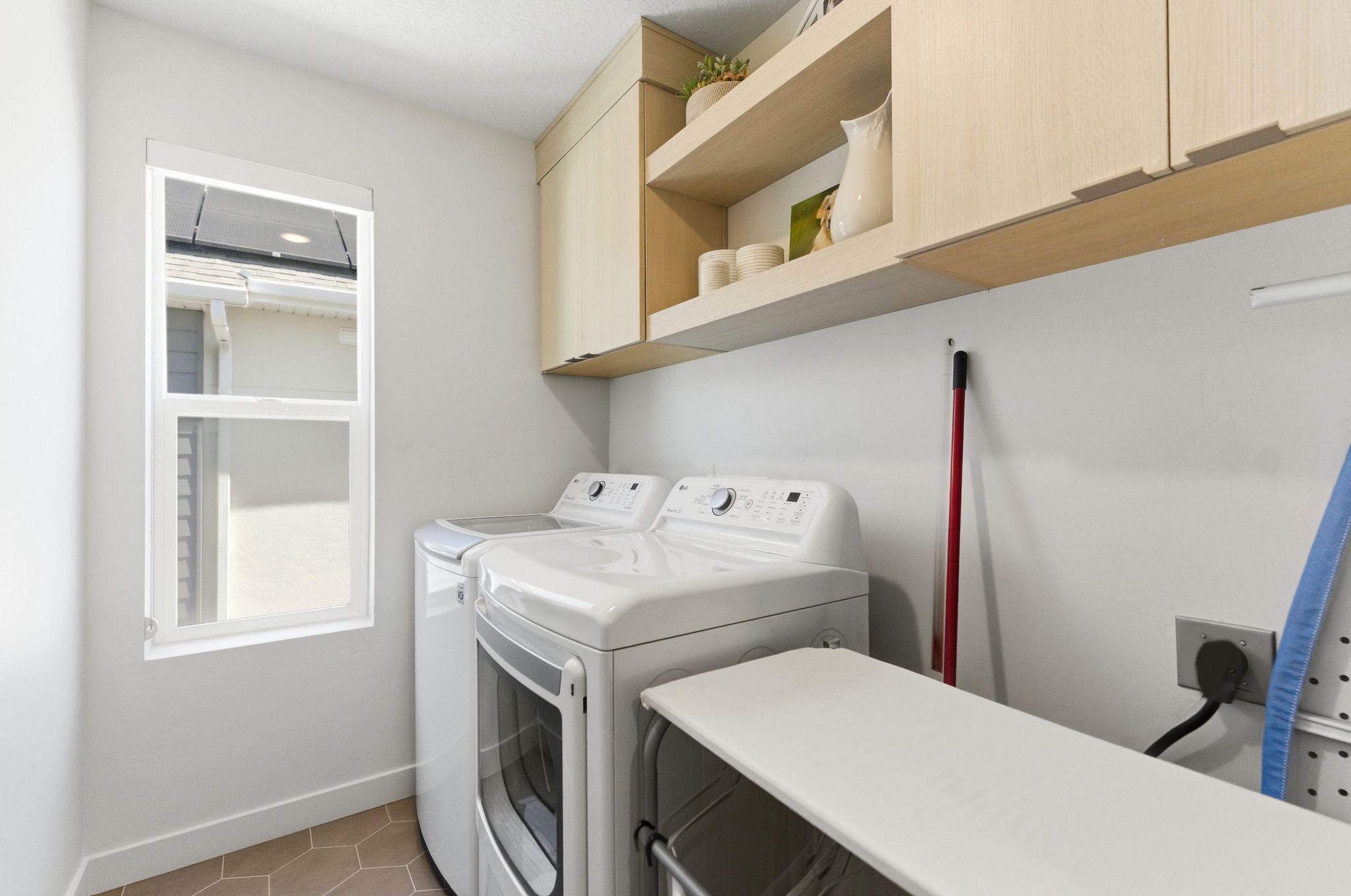 Utility room with a window, hexagon tile flooring, and light wood-finish cabinetry