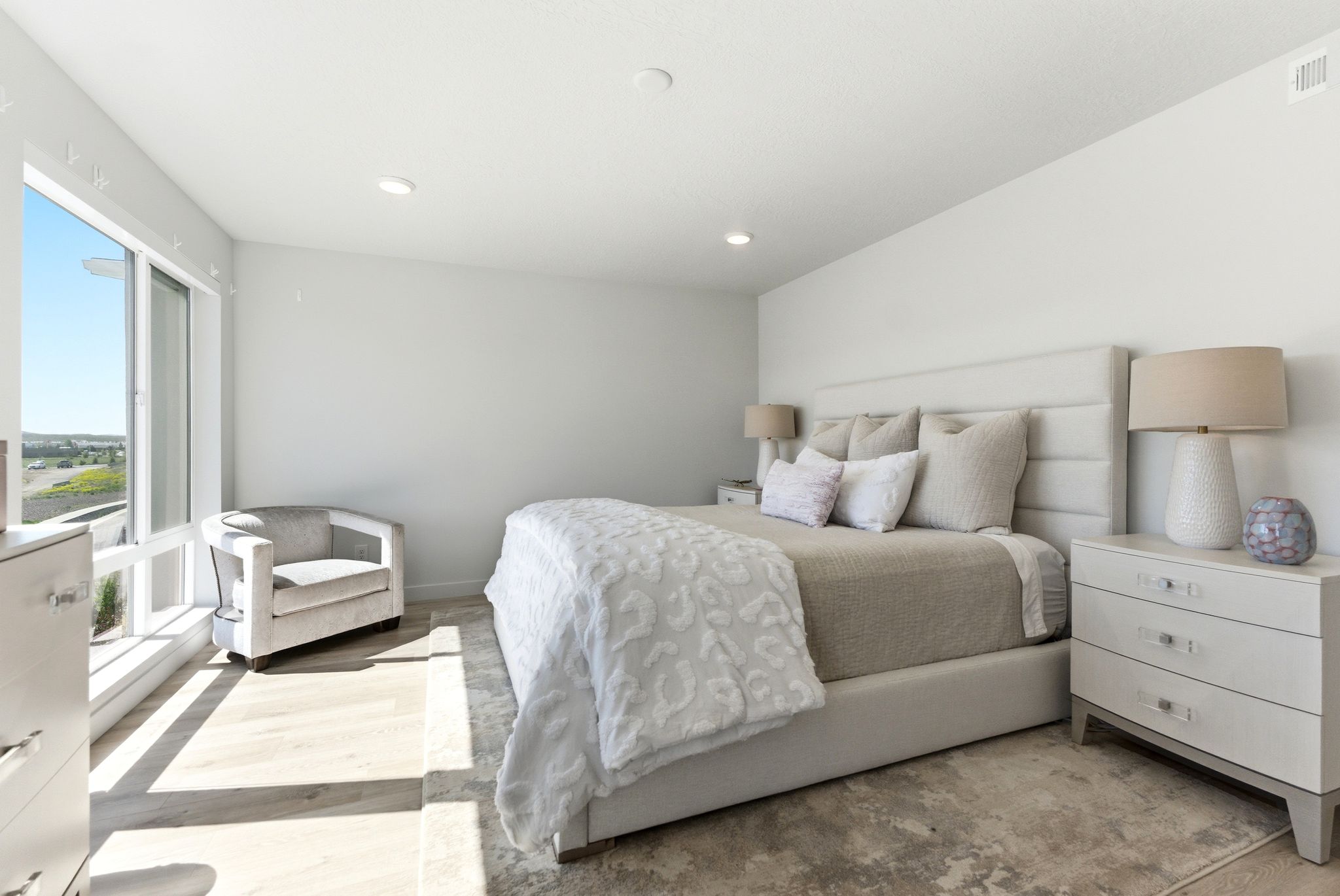 Spacious bedroom featuring light wood-finish flooring, a large window, recessed lighting, a built-in upholstered headboard, and built-in nightstands