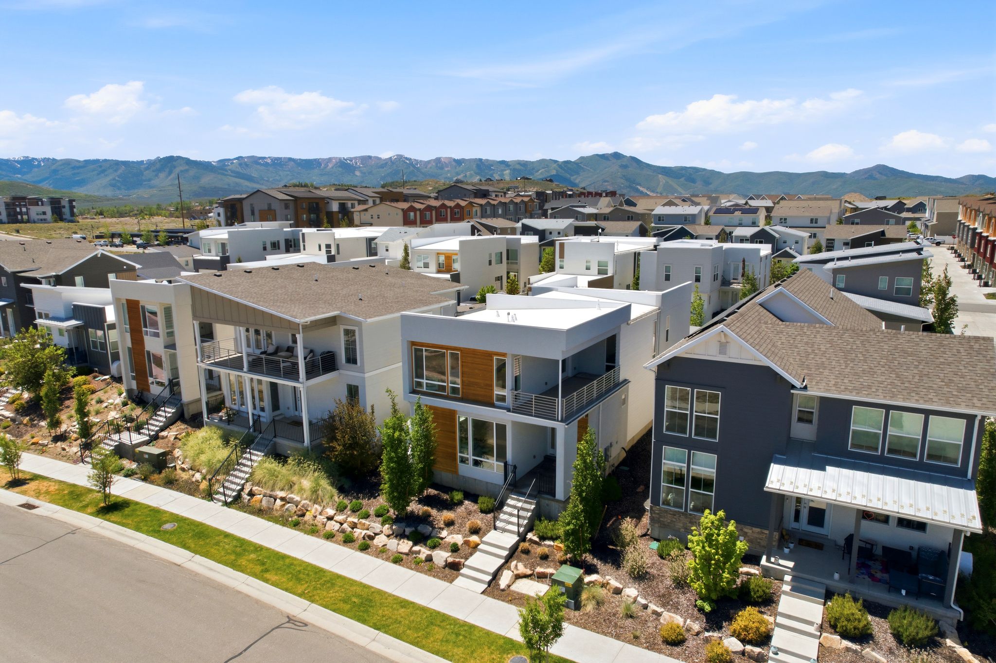 Contemporary architectural design featuring a prominent balcony, multiple large windows, a flat roofline, a sloped roofline, and a tiered rock and plant hardscape