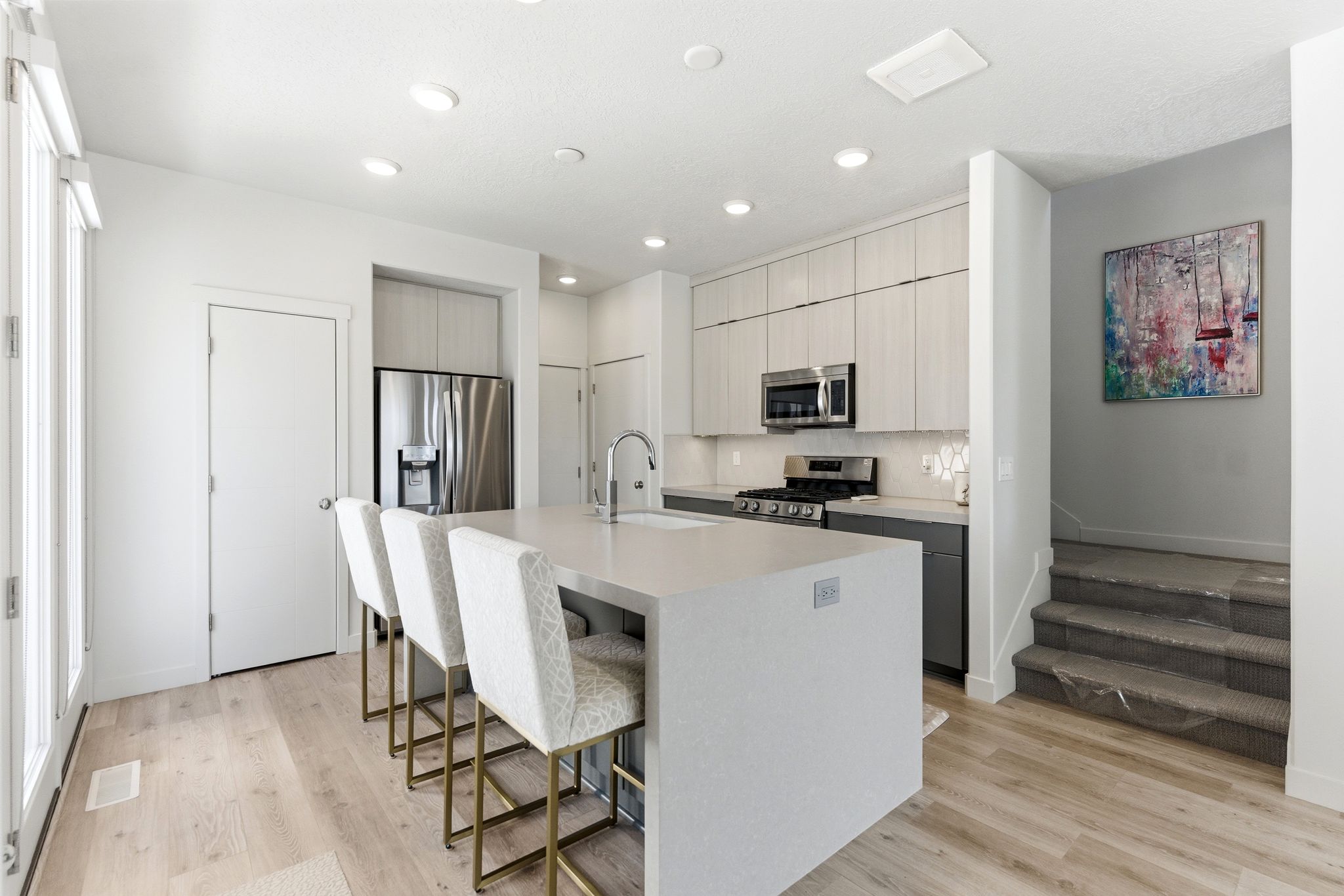 Modern kitchen featuring a waterfall-edge island with seating, stainless steel appliances, light-toned wood-finish flooring, recessed lighting, and a neutral color palette