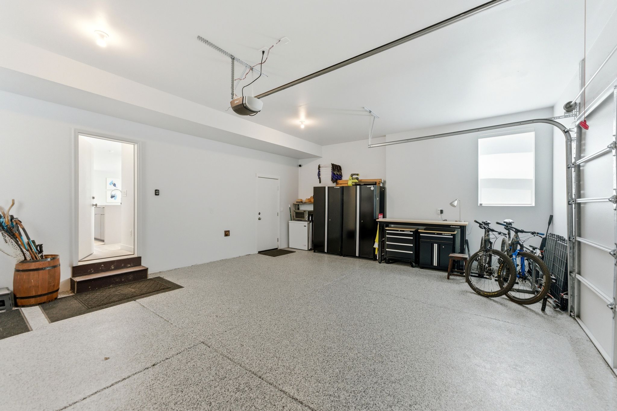 Garage featuring a speckled epoxy floor, white painted walls, overhead lighting, and a roll-up garage door with tracks