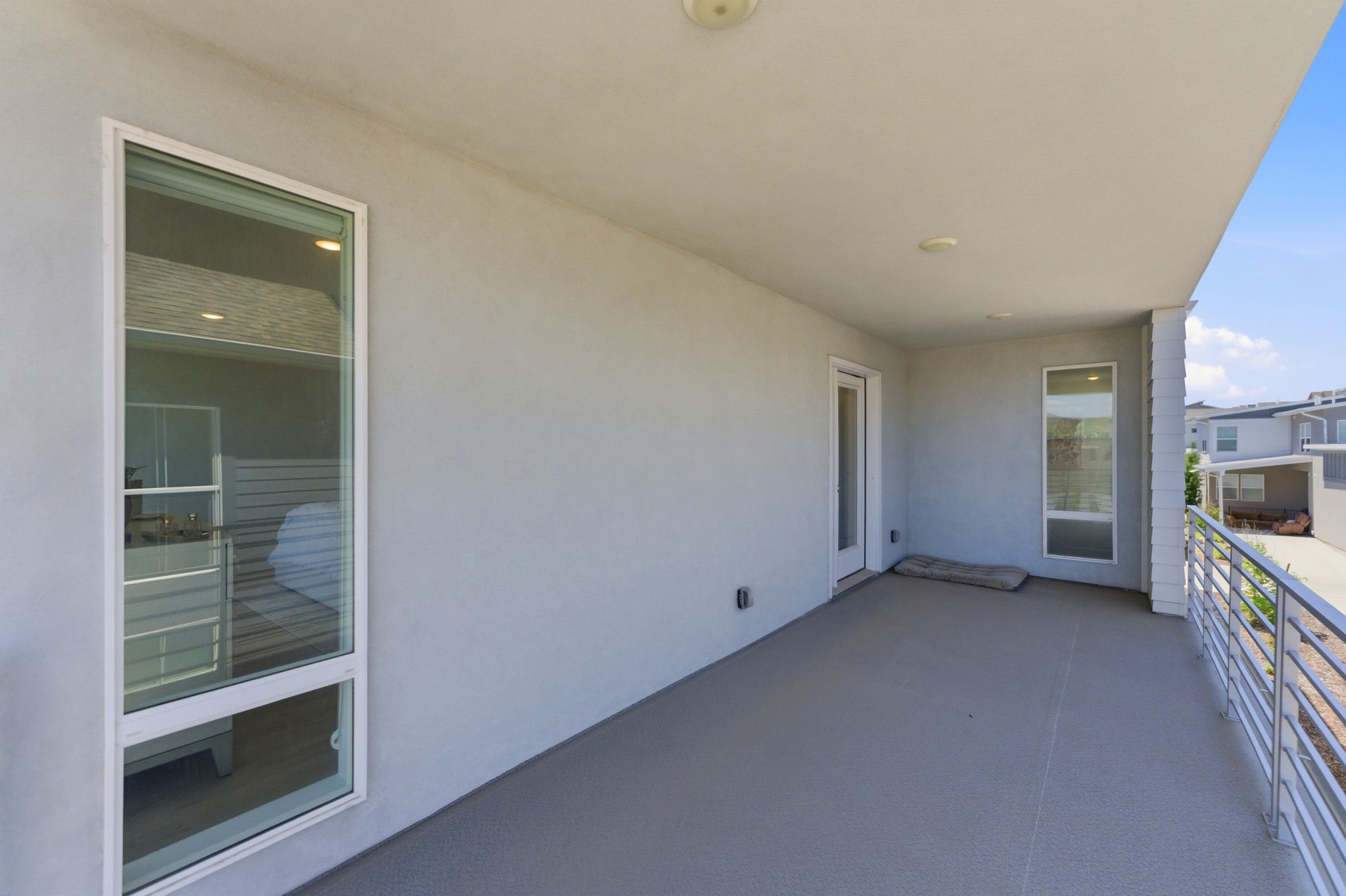 Expansive covered balcony featuring a light gray concrete surface, a white stucco exterior finish, recessed lighting, and white-framed windows