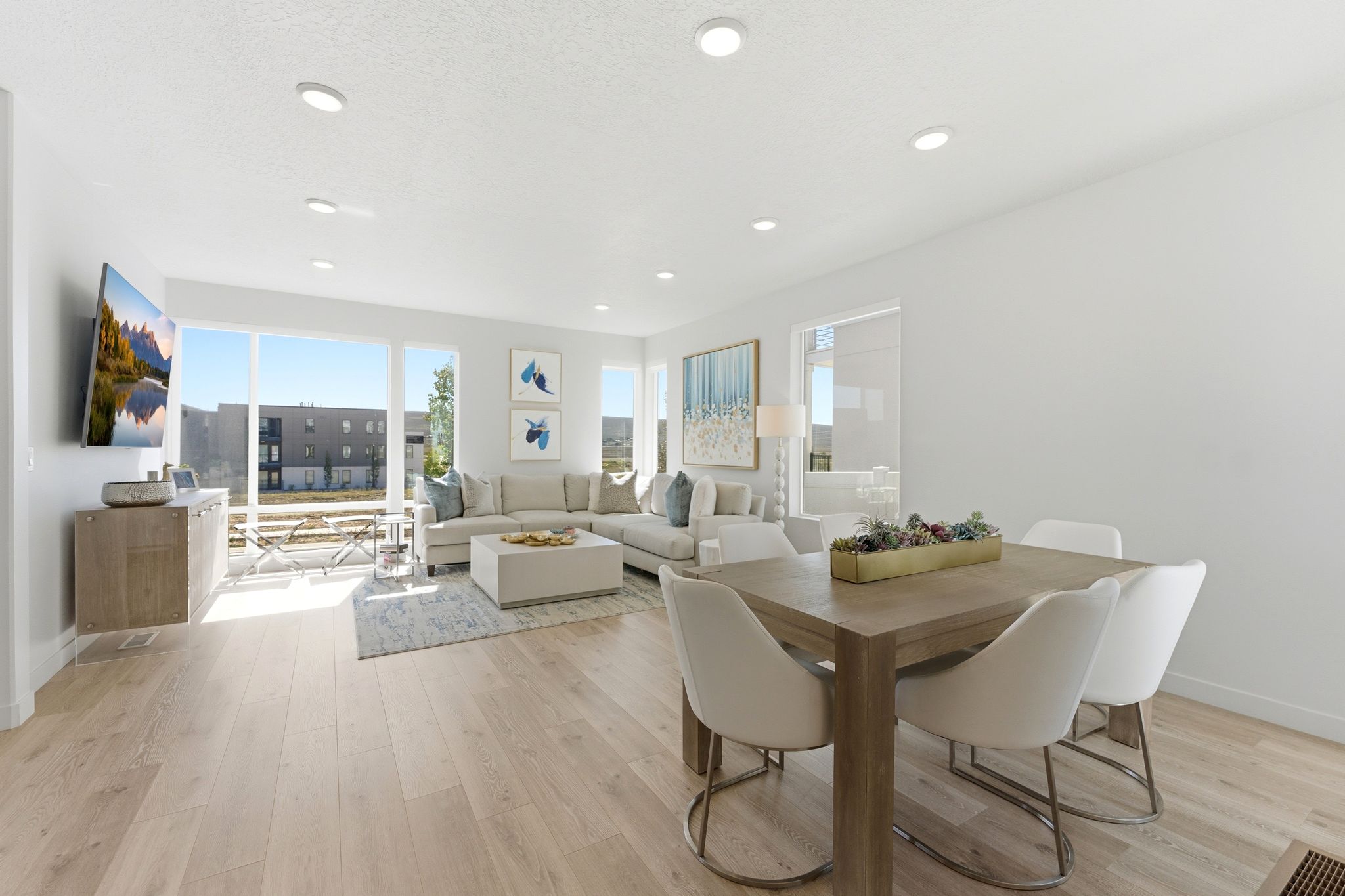 Open-concept living and dining area featuring light wood-finish flooring, recessed lighting, and expansive windows