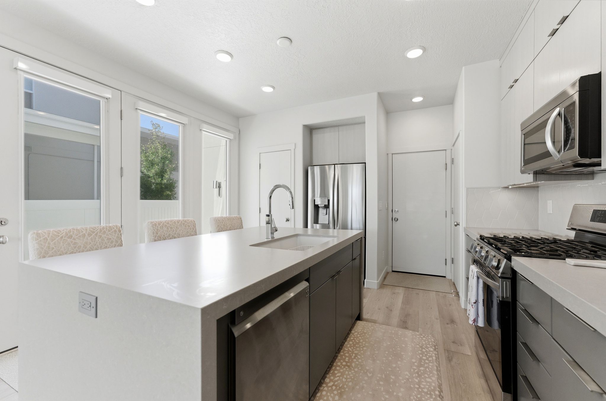 Kitchen featuring a large central island with integrated sink, stainless steel appliances, light wood-finish flooring, white cabinetry, and recessed lighting