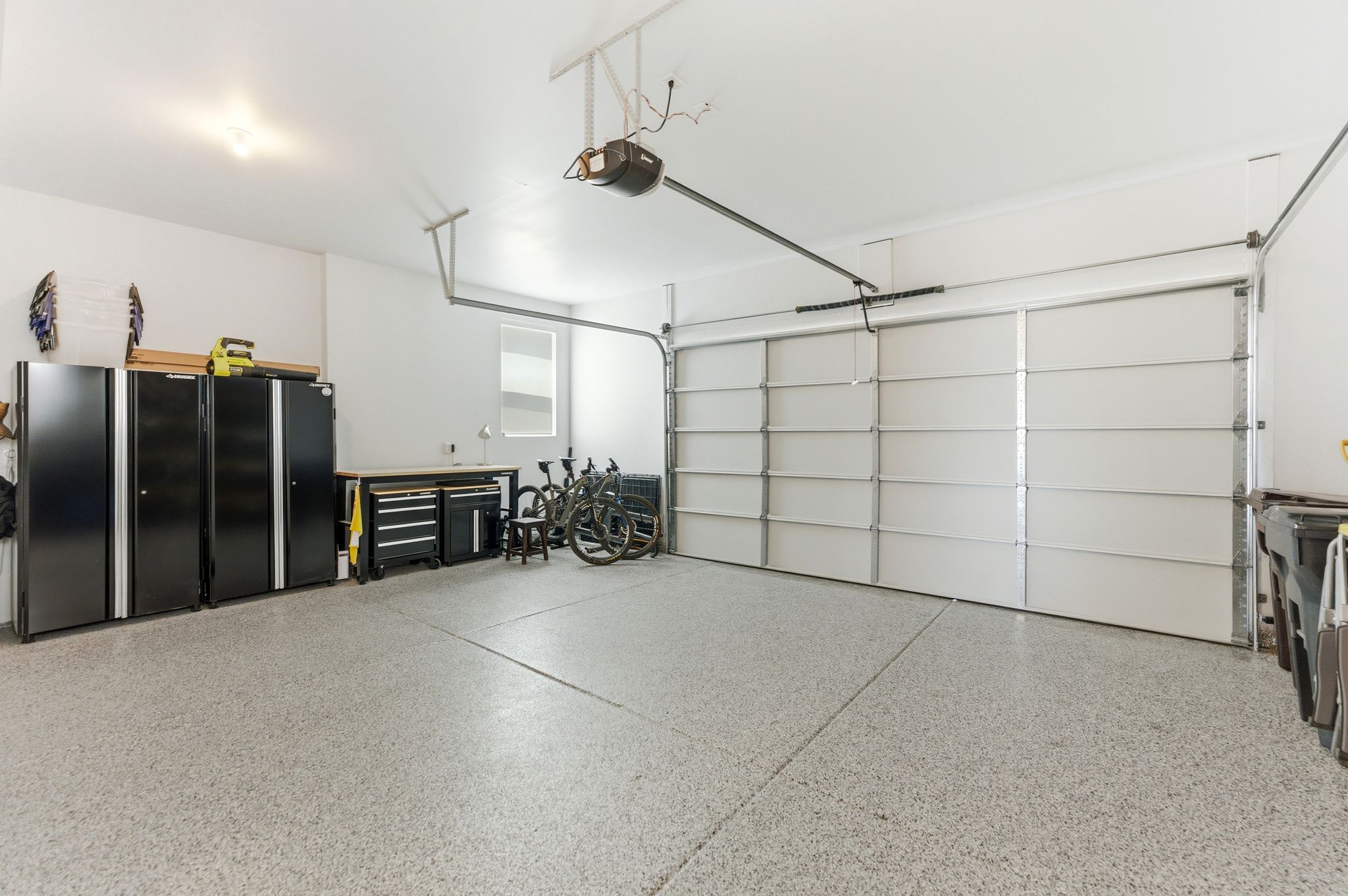 Spacious garage featuring a light-toned epoxy floor, an automatic overhead garage door, a window with horizontal blinds, and overhead lighting