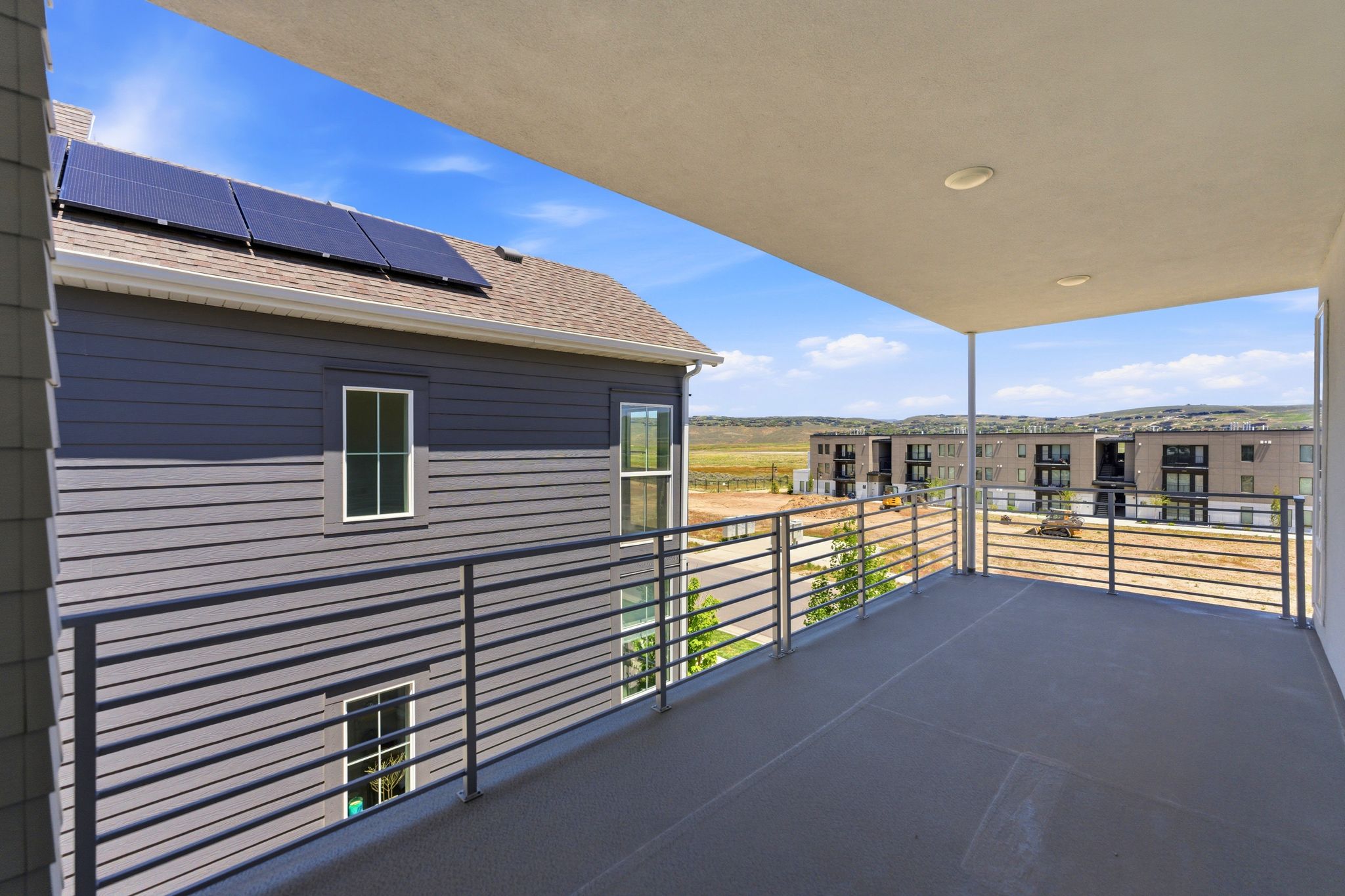 Expansive outdoor balcony featuring a solid ceiling with recessed lighting and a contemporary metal railing