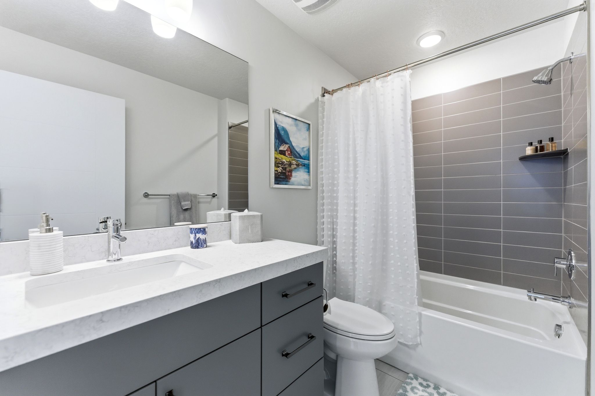 Bathroom featuring a single vanity with a white countertop, an undermount sink, and gray cabinetry with black hardware