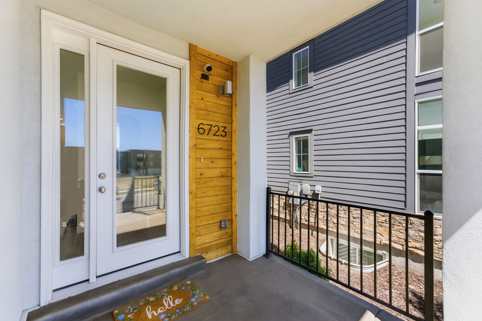 Entryway featuring a glass-paneled door with an adjacent sidelight, plank wood accent wall with modern house numbers, and a contrasting gray exterior with white trim