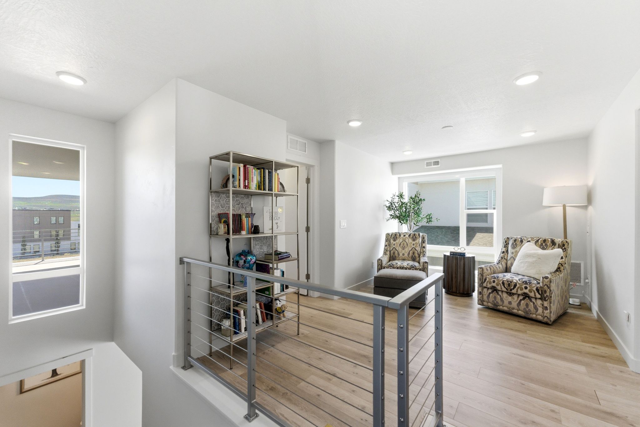 Upper-level landing featuring light wood-finish flooring, recessed lighting, and a contemporary metal railing