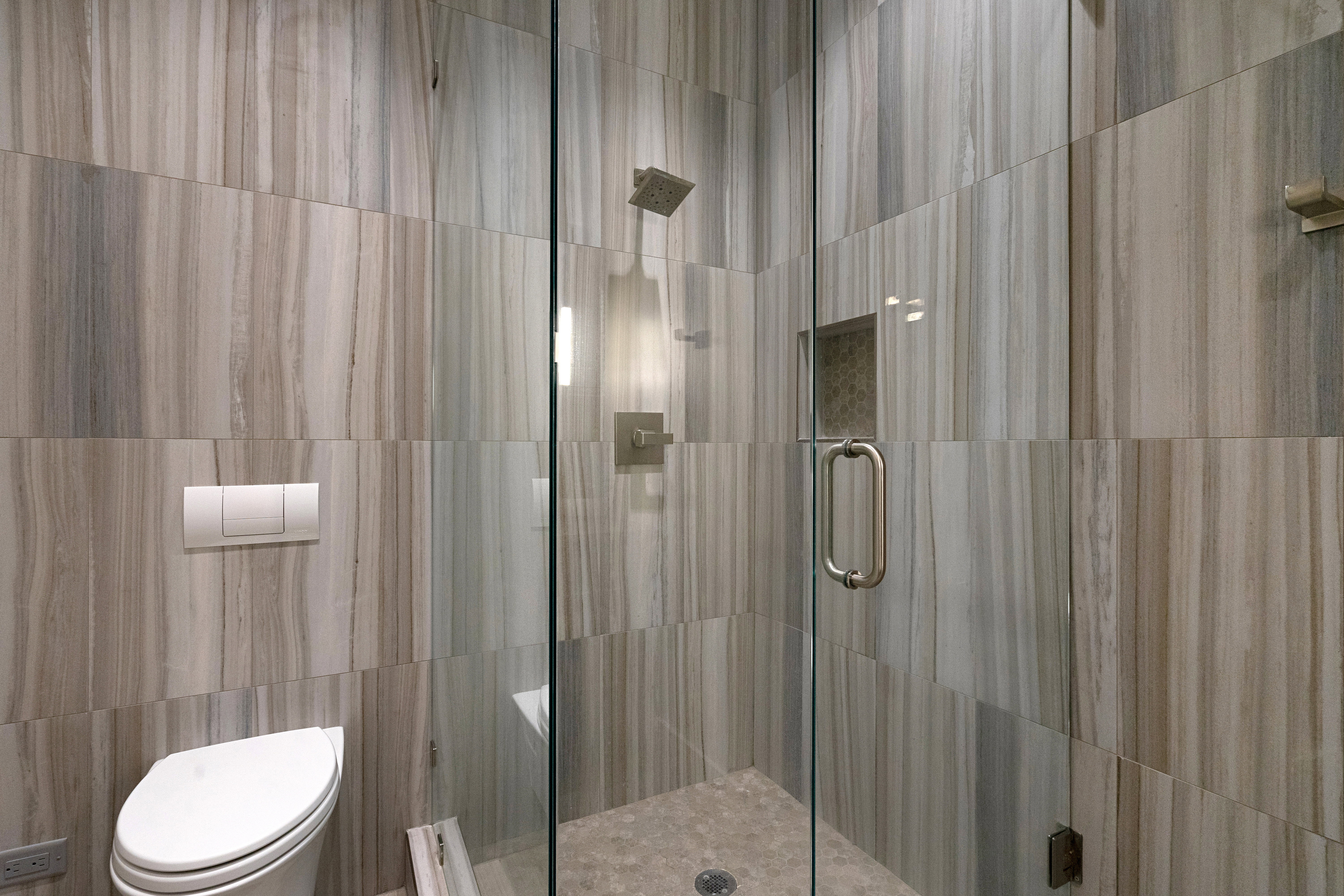Glass-enclosed shower with a recessed niche and rain shower head, featuring large format wall tiles and a pebble floor
