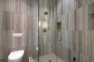Glass-enclosed shower with a recessed niche and rain shower head, featuring large format wall tiles and a pebble floor