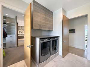 Dedicated laundry area featuring modern front-load appliances, wood-finish cabinetry, and a light-toned countertop
