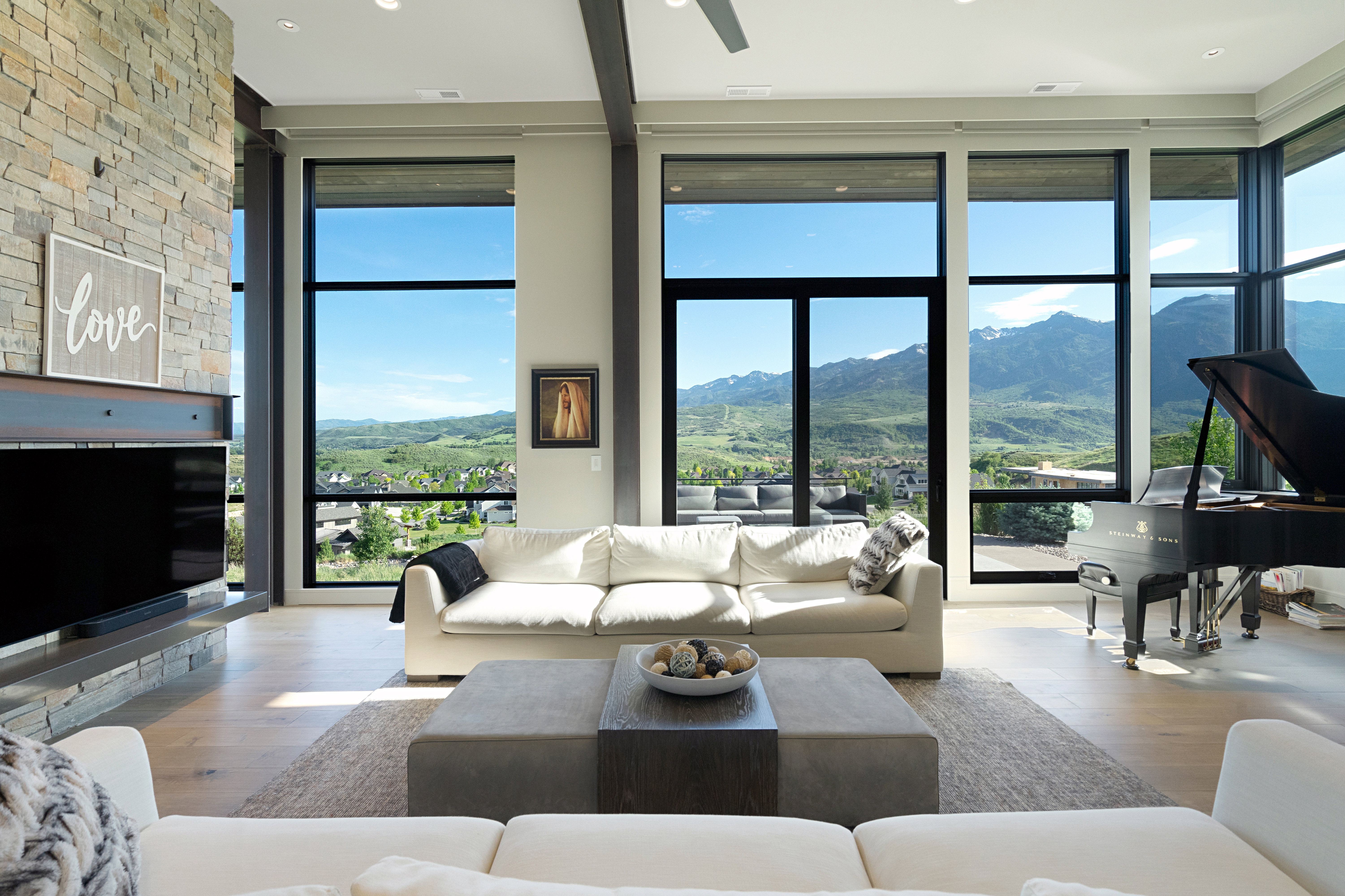 Contemporary living area featuring expansive floor-to-ceiling windows, light wood-finish flooring, and a floor-to-ceiling stone-clad fireplace