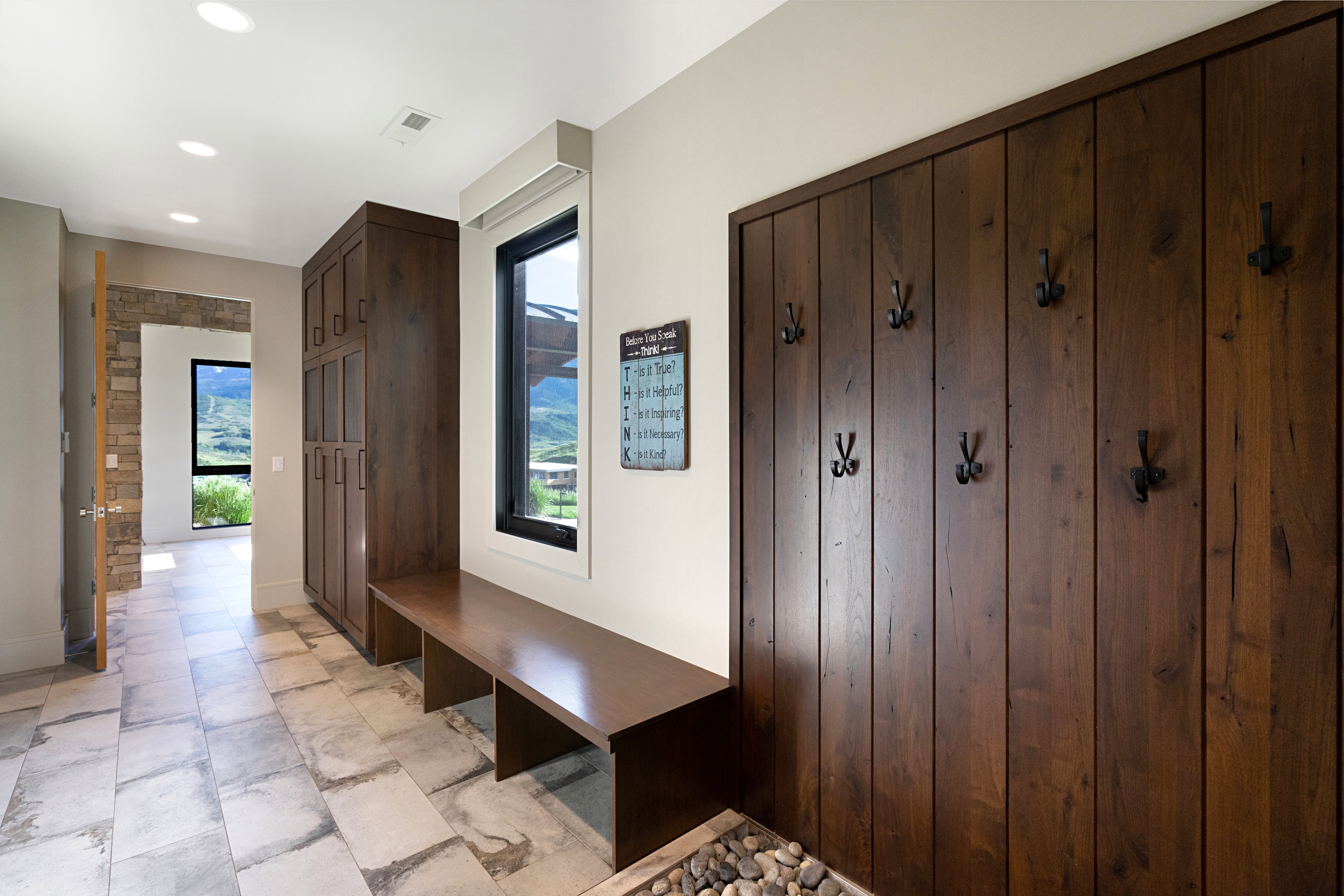 Mudroom entry featuring a built-in wood-finish bench, floor-to-ceiling wood-finish paneling with coat hooks, and stone tile flooring