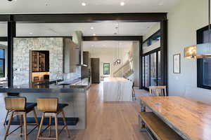 Open-concept kitchen featuring an oversized island with waterfall countertop, stone accent wall, integrated stainless steel appliances, and wide plank wood-finish flooring