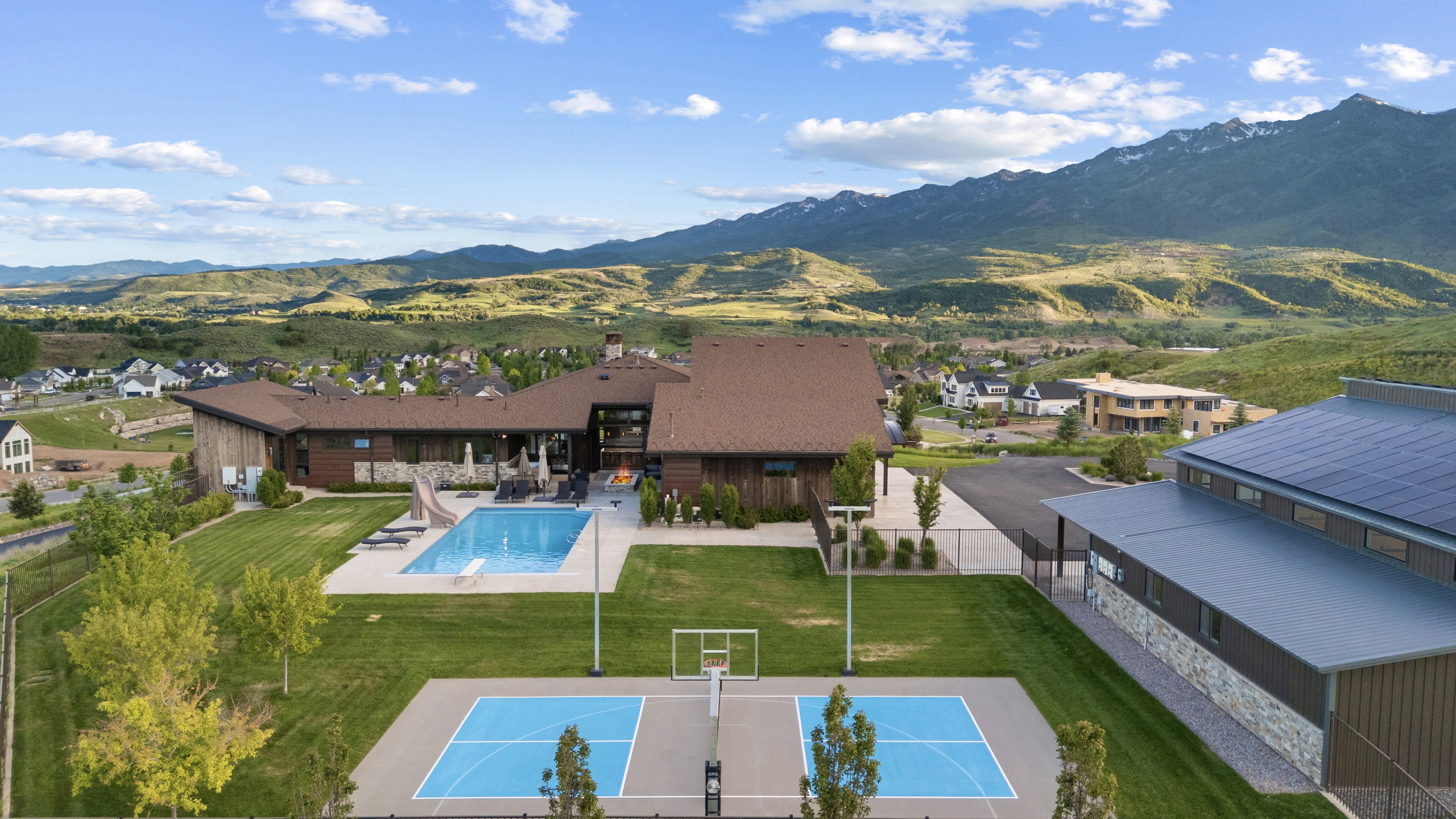 Expansive property featuring a large swimming pool with a diving board, a separate sport court, and a contemporary multi-level residence with extensive outdoor patio space