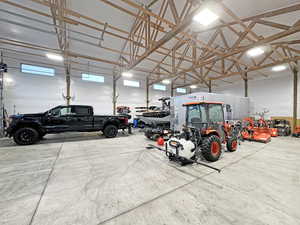 Spacious utility building featuring a high exposed timber frame ceiling, concrete flooring, ample overhead lighting, and multiple windows