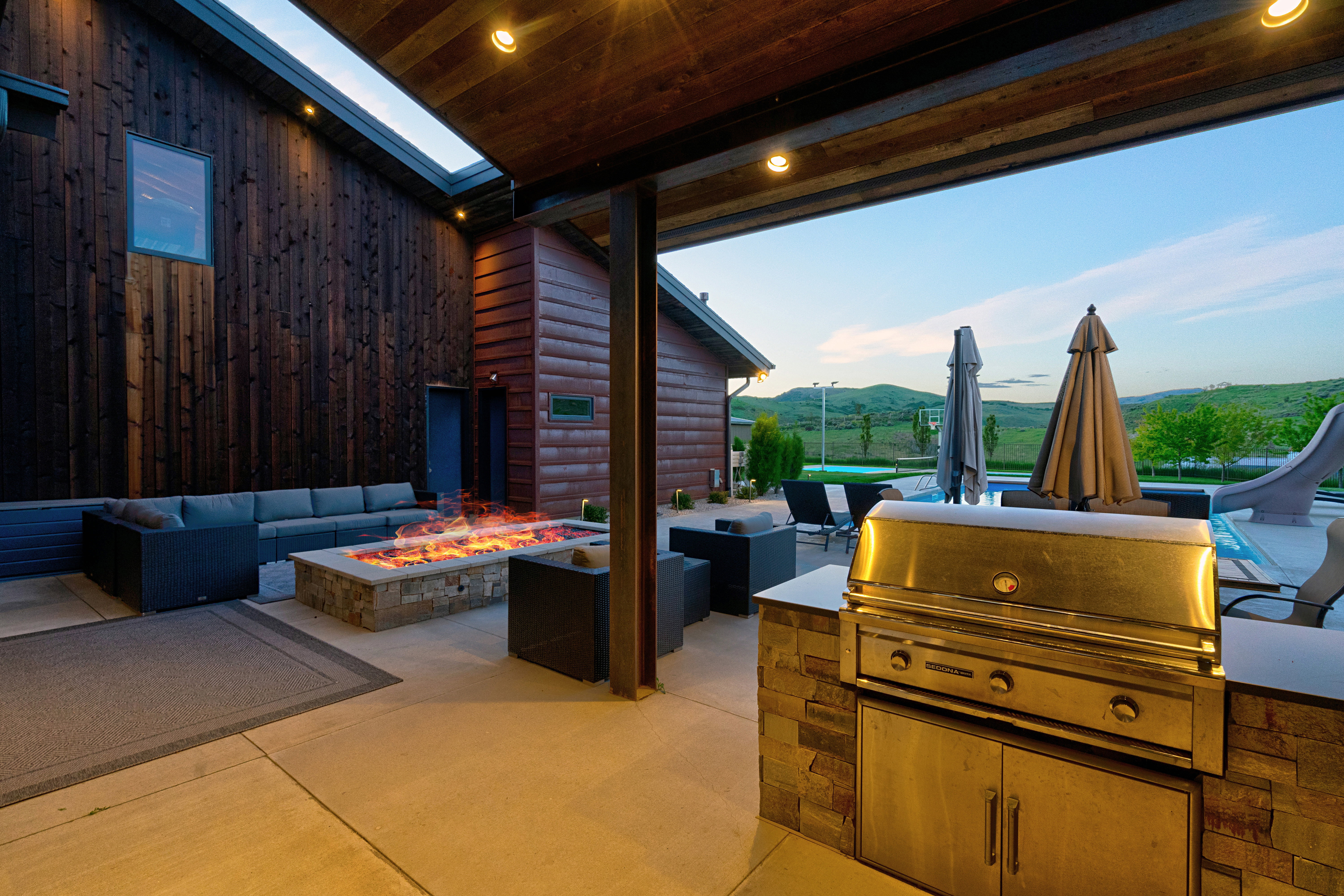 Expansive covered patio featuring a built-in stone fire pit, wood-paneled ceiling with recessed lighting, and a built-in outdoor grill with stone accents and stainless steel cabinetry