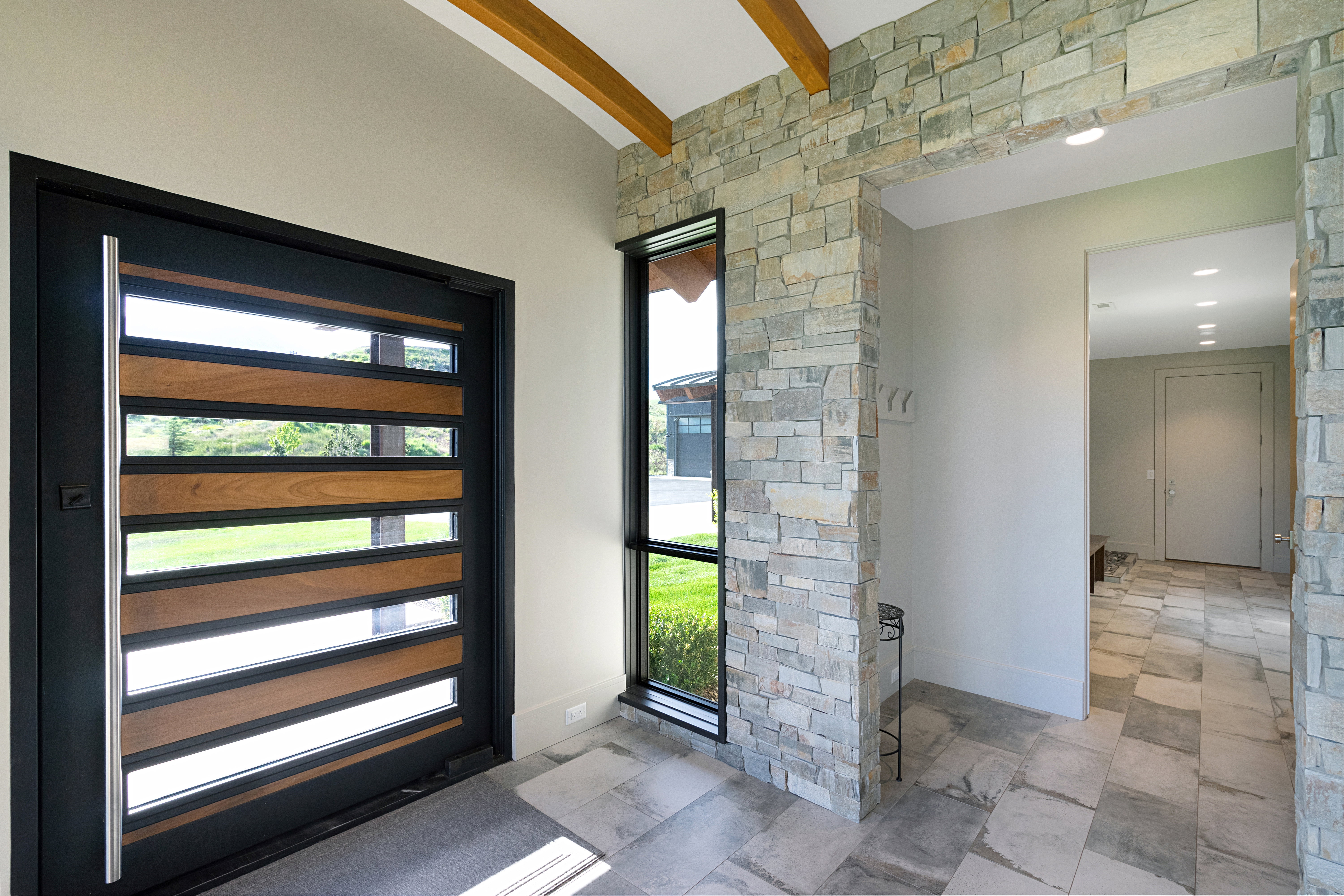 Modern entry featuring a dark-framed door with horizontal wood and glass inserts, a full-height sidelight, and a stacked stone wall accent