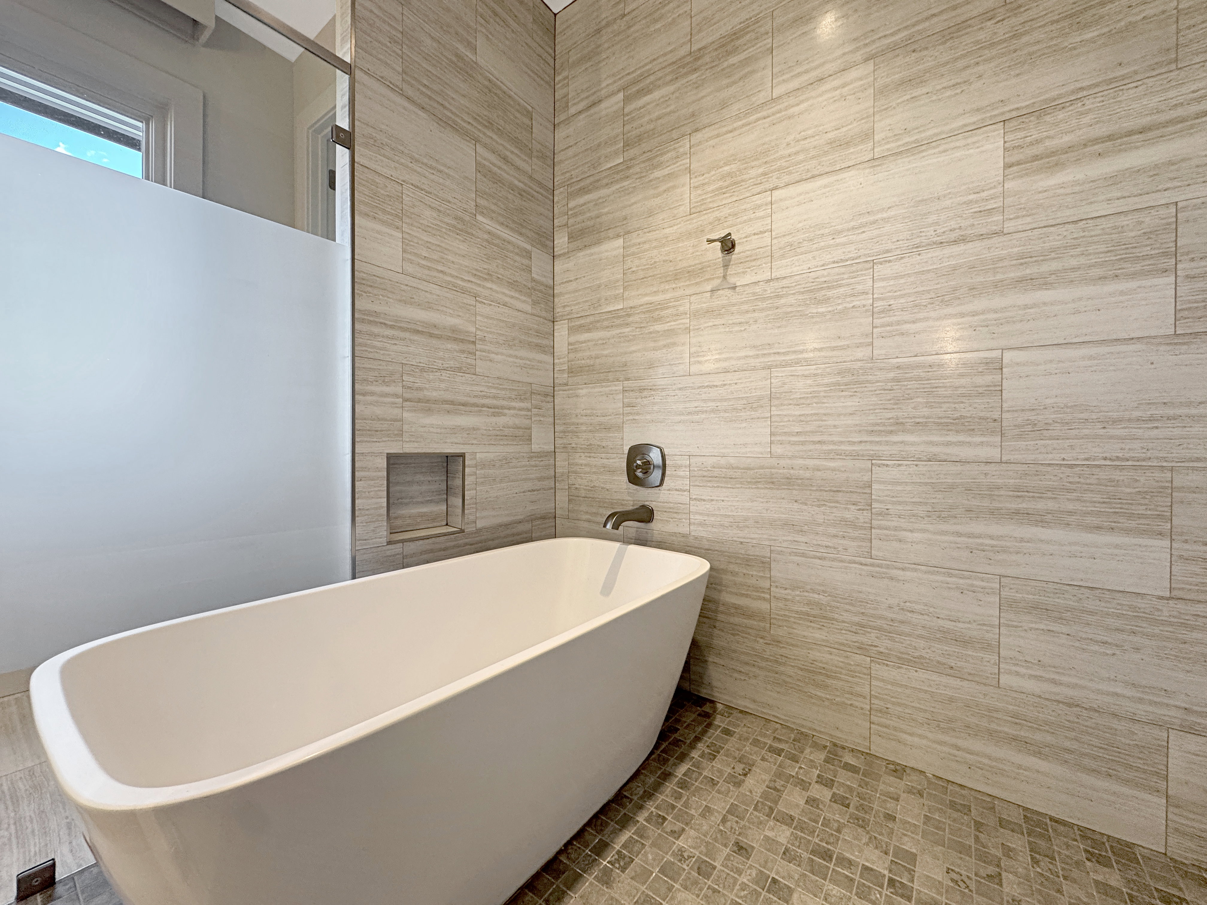 Freestanding soaking tub with a tiled surround, recessed shower niche, and mosaic tile flooring