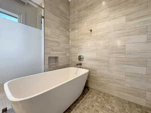 Freestanding soaking tub with a tiled surround, recessed shower niche, and mosaic tile flooring