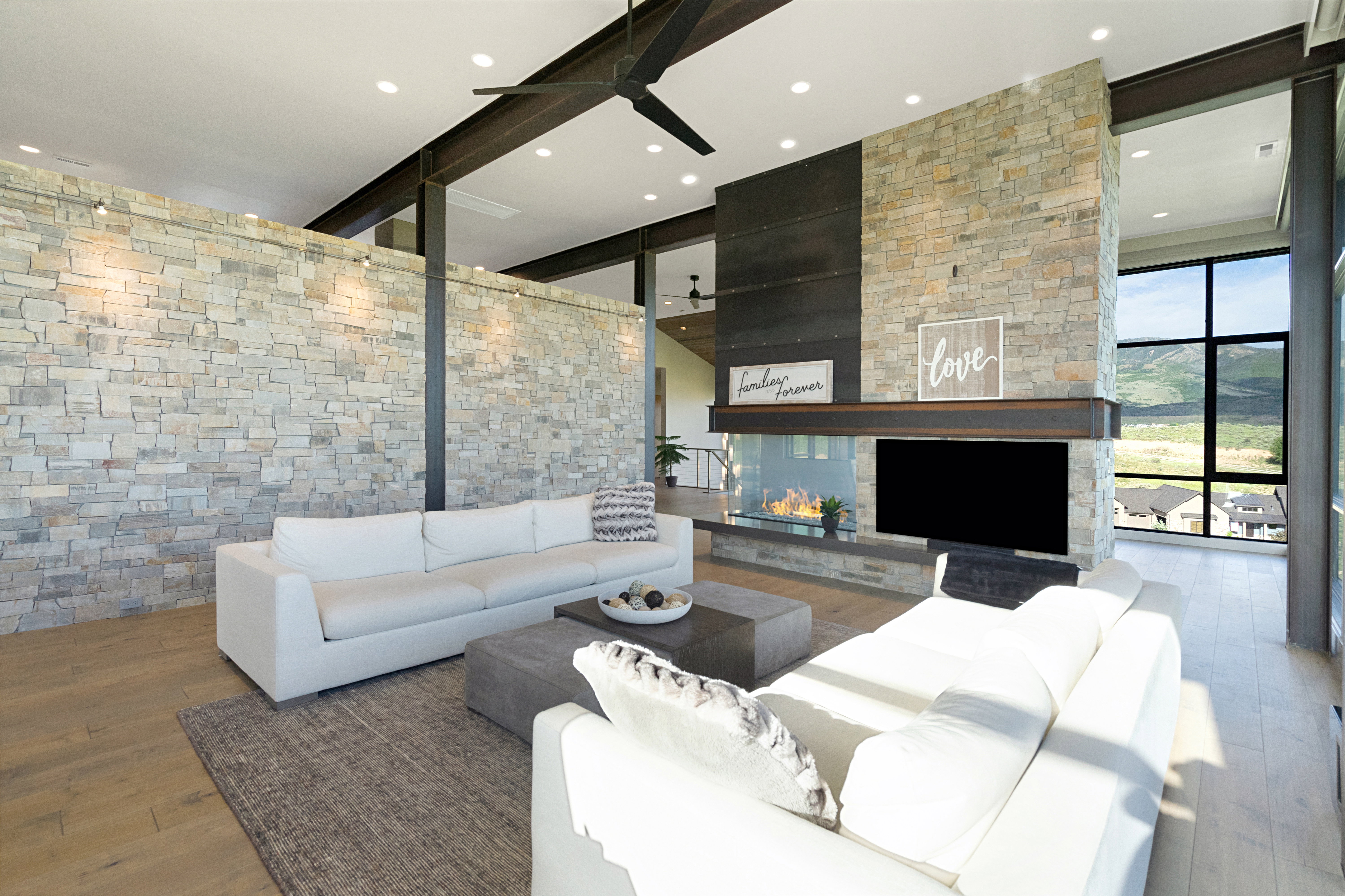 Spacious living area featuring a stone accent wall, high ceilings with exposed beams, and light wood-finish flooring