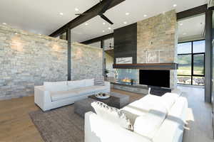 Spacious living area featuring a stone accent wall, high ceilings with exposed beams, and light wood-finish flooring