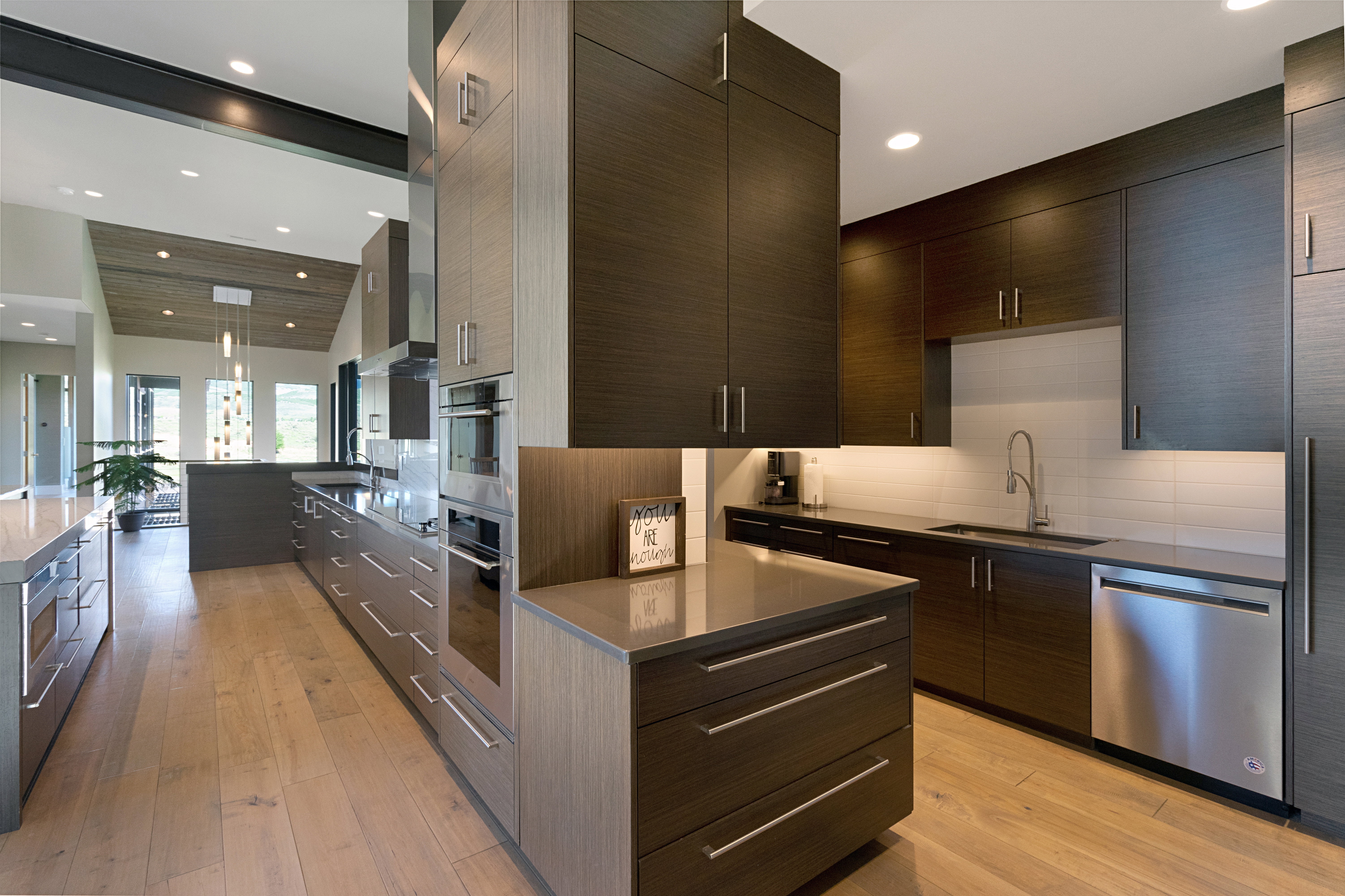 Modern kitchen featuring wood-finish flooring, two-tone cabinetry, stainless steel appliances, integrated oven, and a contemporary range hood