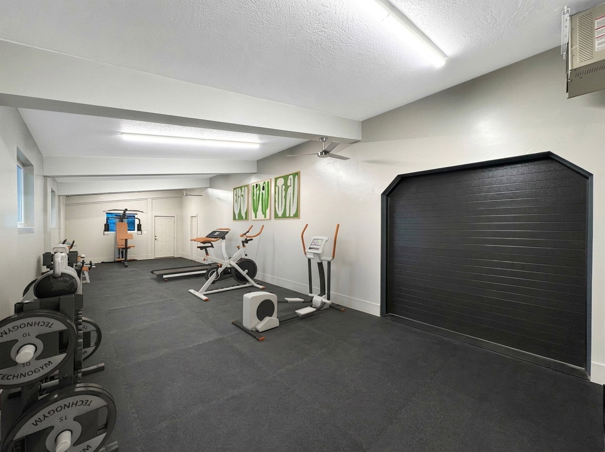 Dedicated fitness space featuring resilient black flooring, multiple windows providing natural light, and ample ceiling-mounted lighting