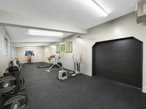 Dedicated fitness space featuring resilient black flooring, multiple windows providing natural light, and ample ceiling-mounted lighting