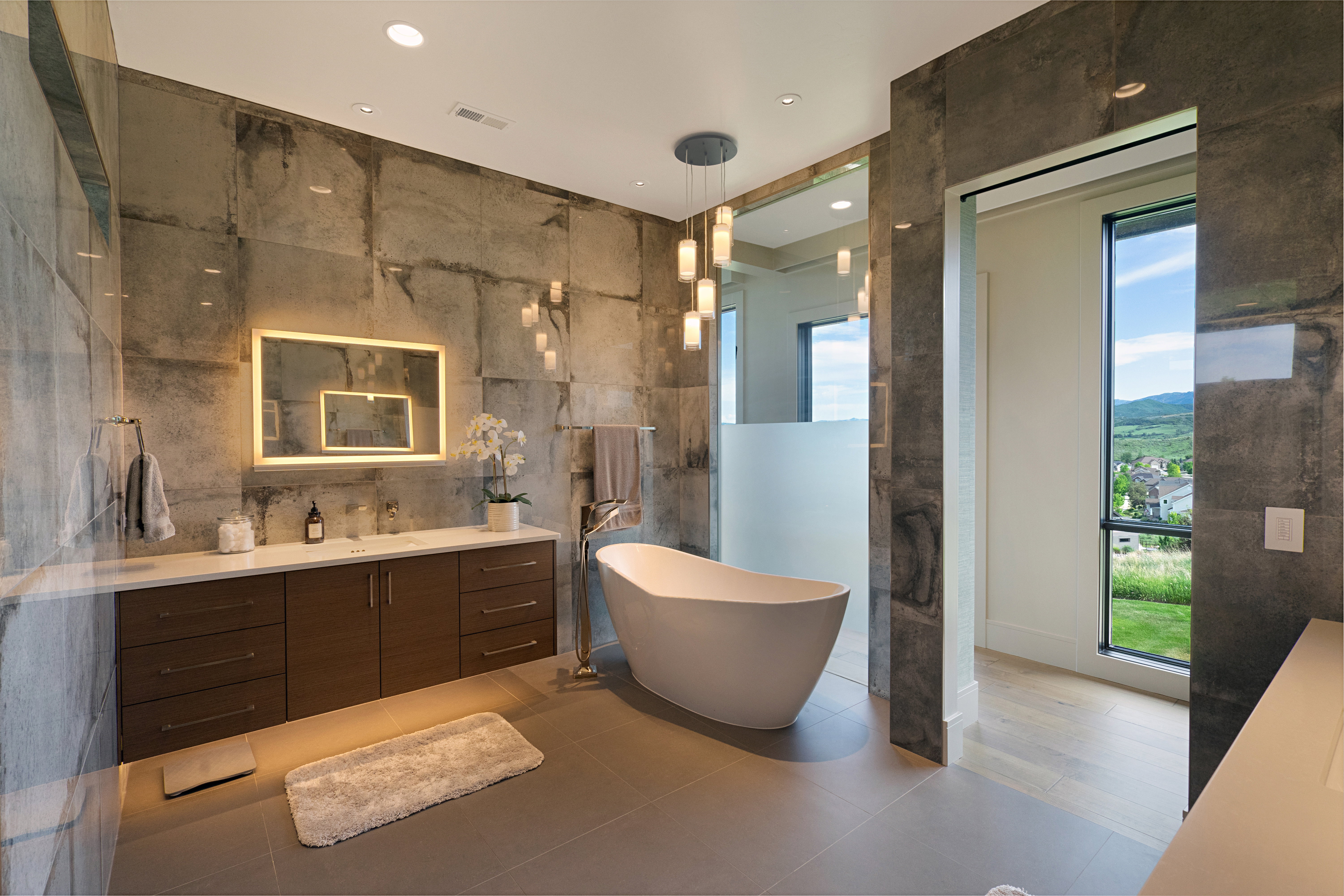 Contemporary bathroom featuring a freestanding soaking tub, a double vanity with an illuminated mirror, and large format wall and floor tiling