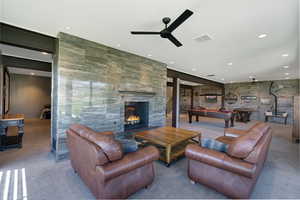 Spacious lounge area featuring a large stone fireplace, recessed lighting, ceiling fans, and exposed structural beams