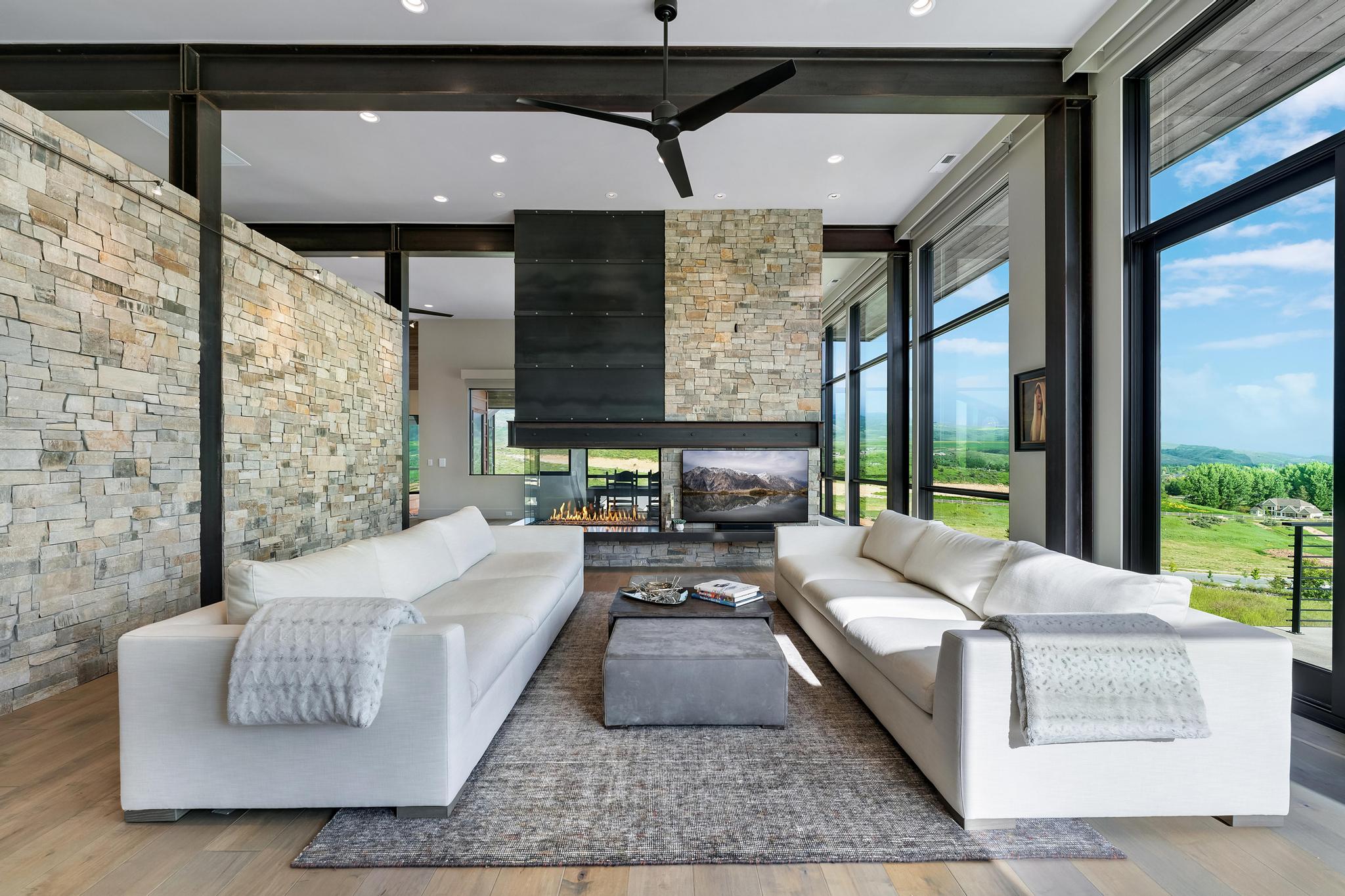 Living space with full-height stone accent wall, exposed structural beams, and wood-finish flooring