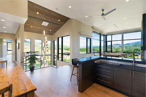 Open-concept living space featuring wood-finish flooring, a vaulted wood-paneled ceiling with recessed lighting and a skylight, and large-format windows with dark frames