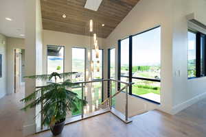 Vaulted wood-finish ceiling above an open landing featuring a multi-tiered chandelier, extensive window placement, stainless steel and cable railing, and wood-finish flooring
