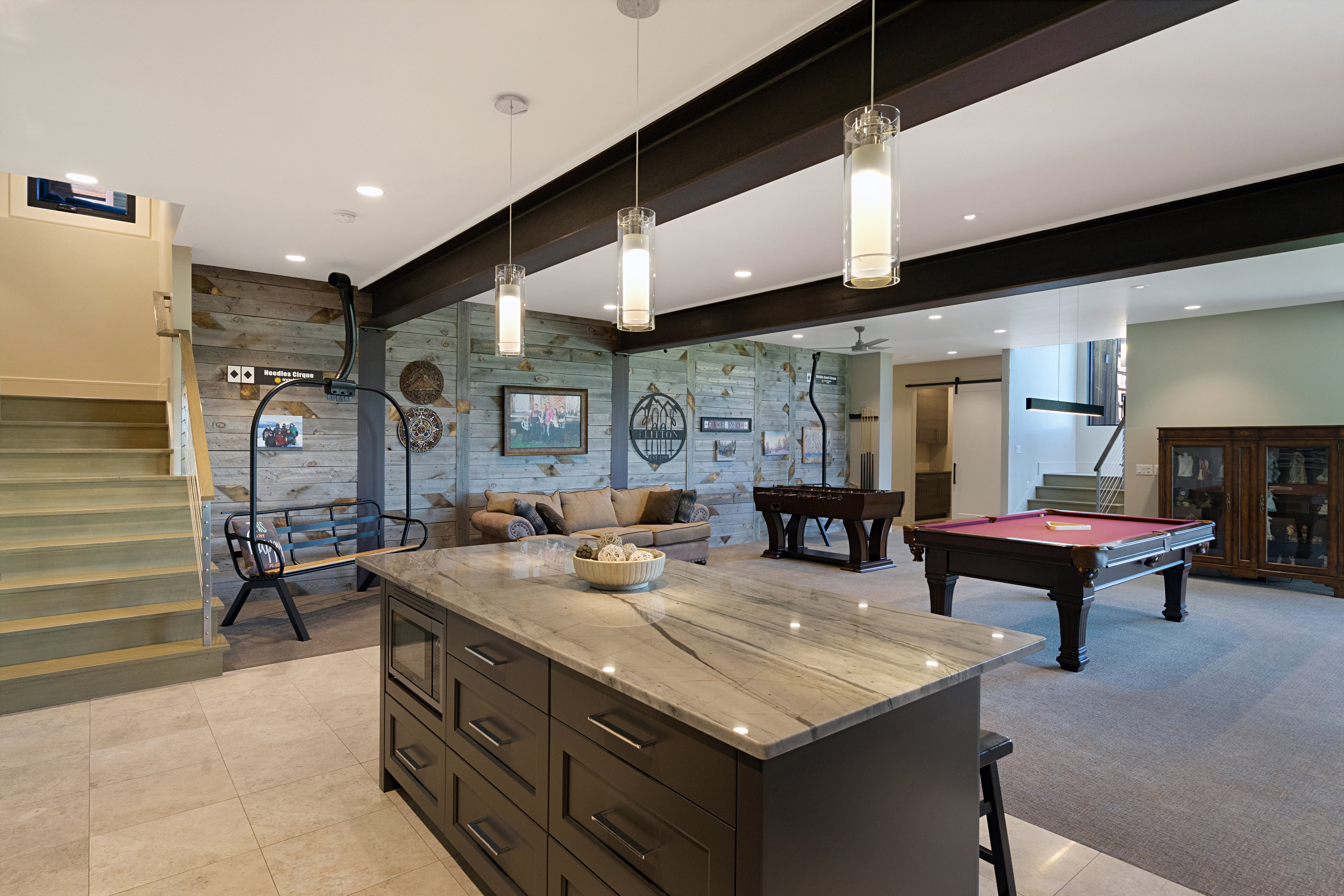 Spacious lower-level entertainment area featuring a large center island with stone countertop, dark wood-finish cabinetry, and built-in microwave