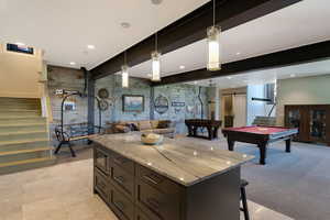 Spacious lower-level entertainment area featuring a large center island with stone countertop, dark wood-finish cabinetry, and built-in microwave