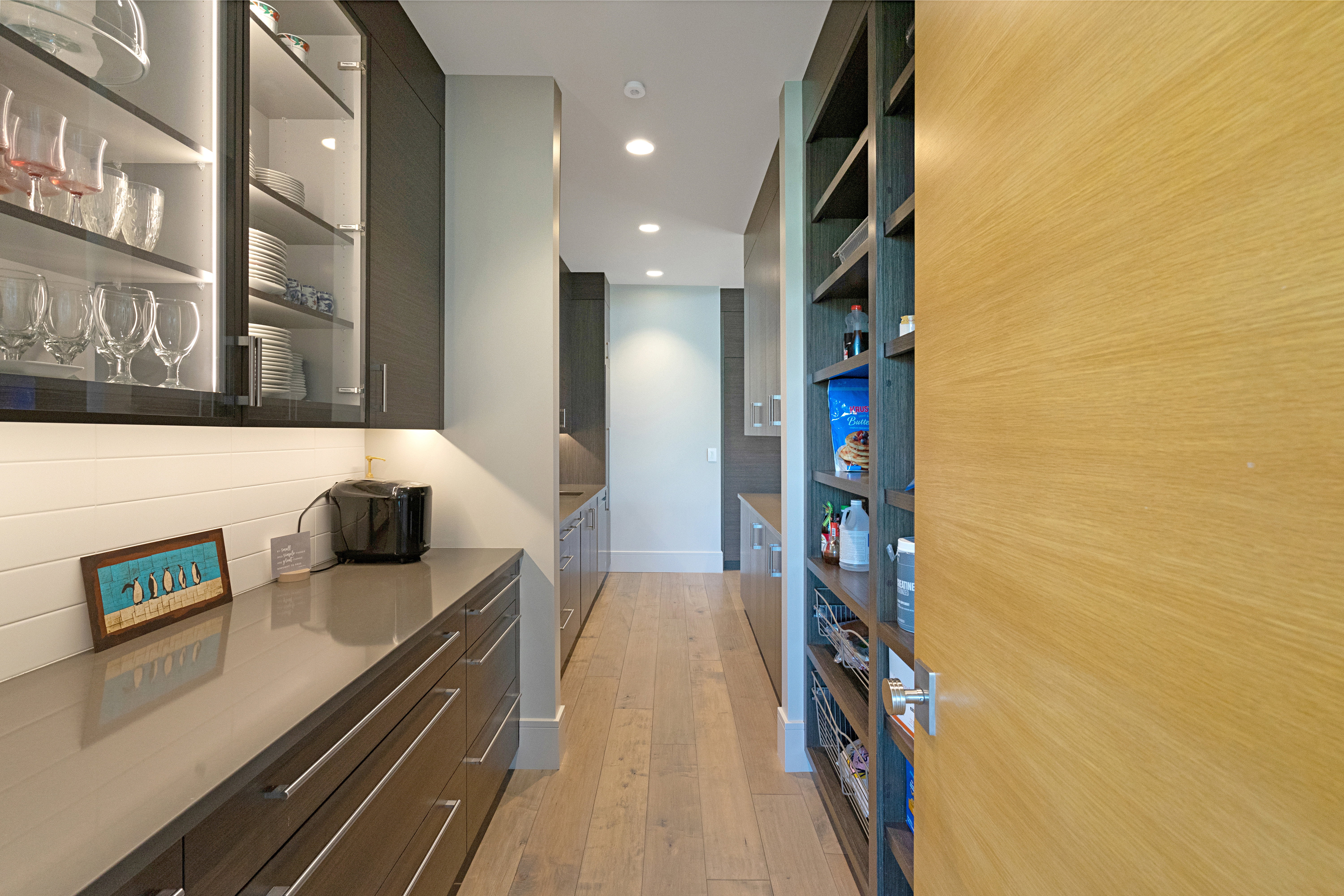 Modern pantry featuring extensive wood-finish shelving, recessed lighting, and light wood-finish flooring
