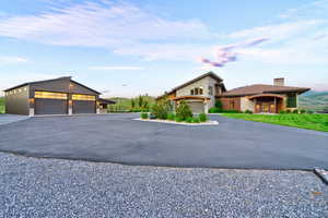 Modern architectural residence with an expansive driveway, a separate multi-car garage, stone and wood-panel exterior accents, and a landscaped property