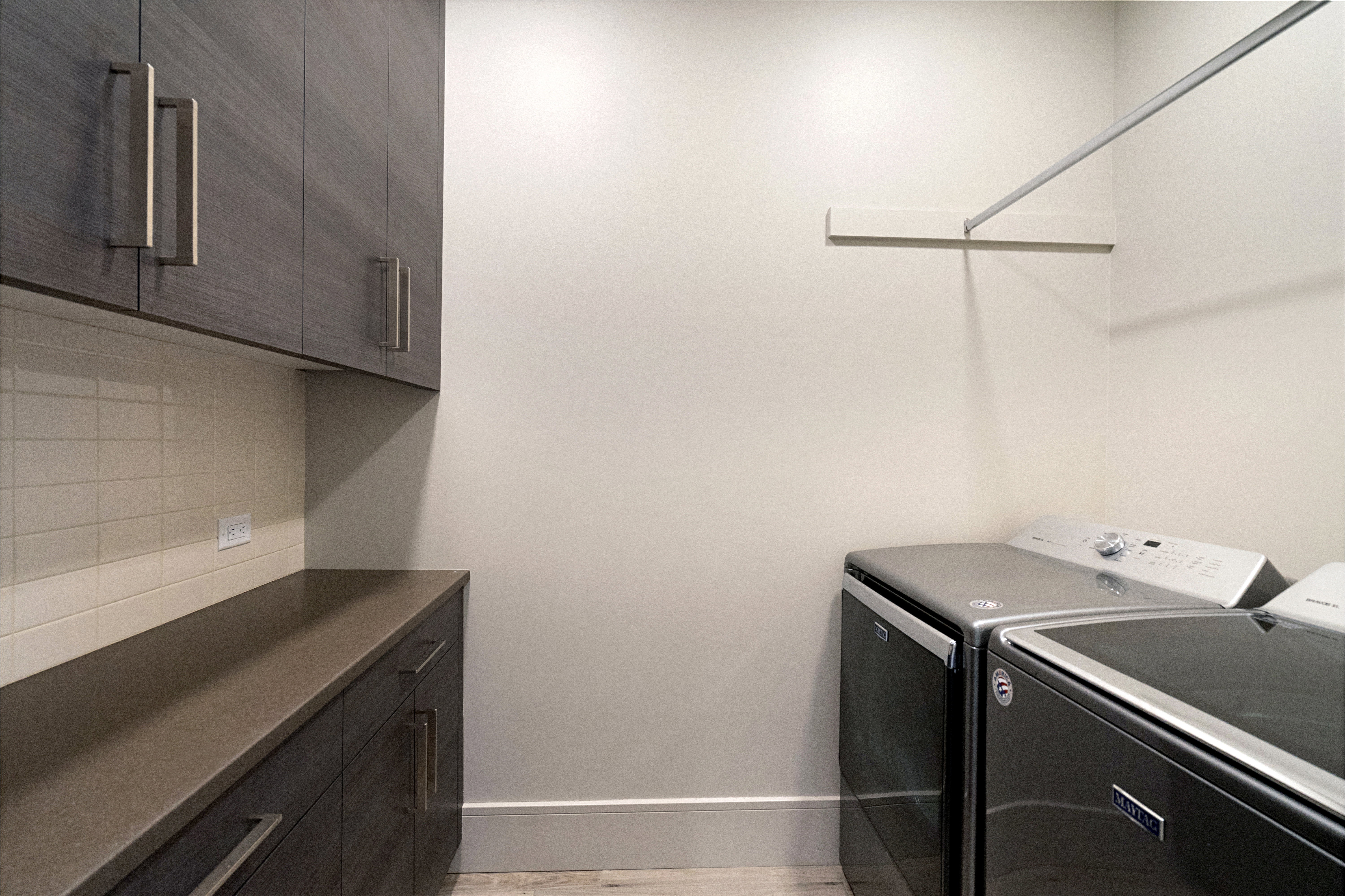 Laundry room featuring wood-finish cabinetry with contemporary hardware, light-colored subway tile backsplash, and a solid surface countertop