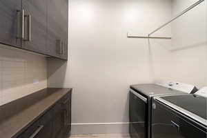 Laundry room featuring wood-finish cabinetry with contemporary hardware, light-colored subway tile backsplash, and a solid surface countertop