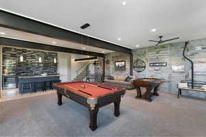 Spacious recreation area featuring a wet bar with a tiled accent wall and built-in cabinetry, exposed structural beams, recessed lighting, and wood-finish wall paneling
