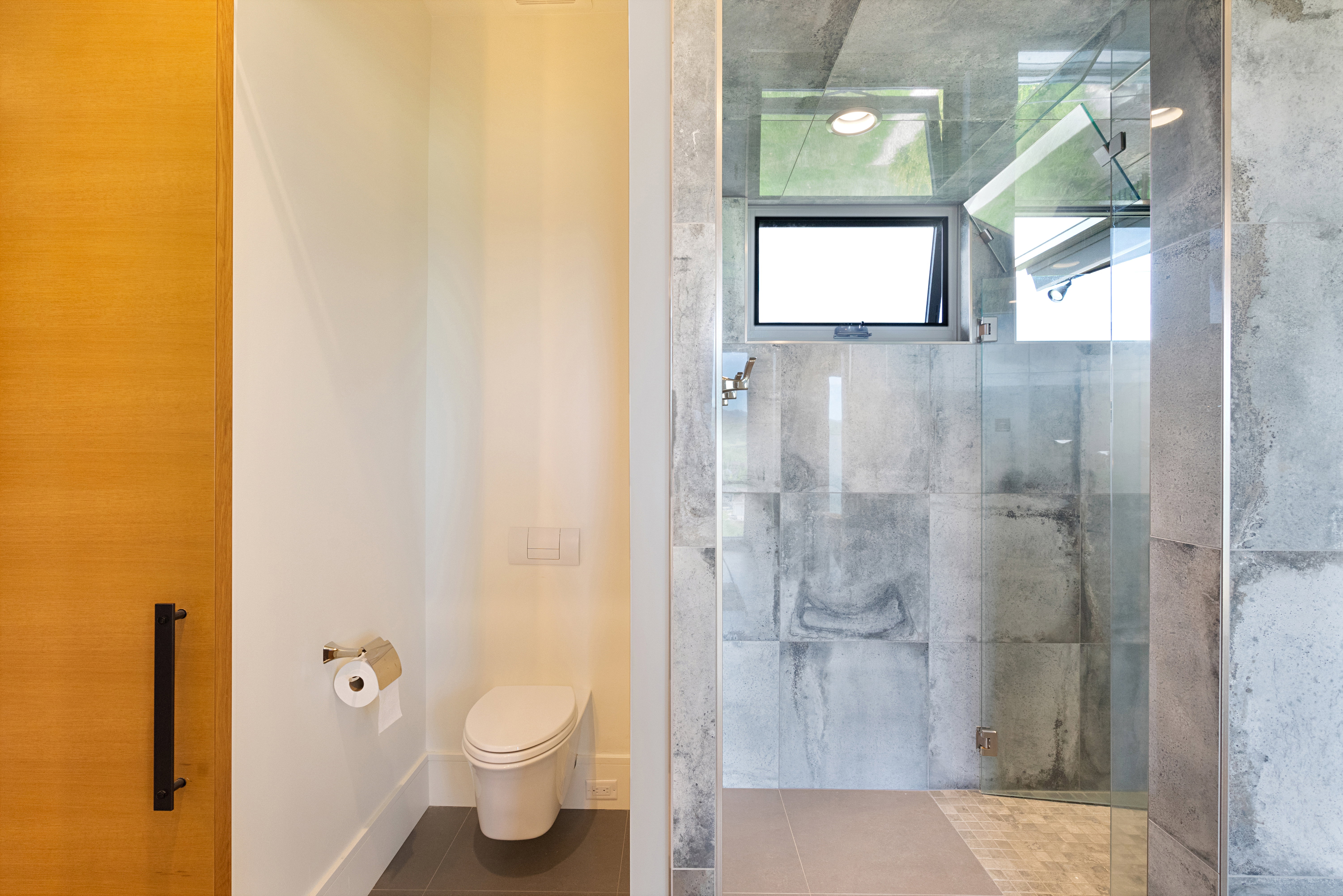 Modern bathroom featuring a frameless glass shower enclosure with large format stone tile walls and a light-colored tile floor