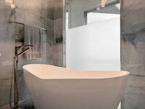 Freestanding soaking tub with a floor-mounted chrome faucet, complemented by large format wall tile and a glass-enclosed shower featuring frosted privacy film