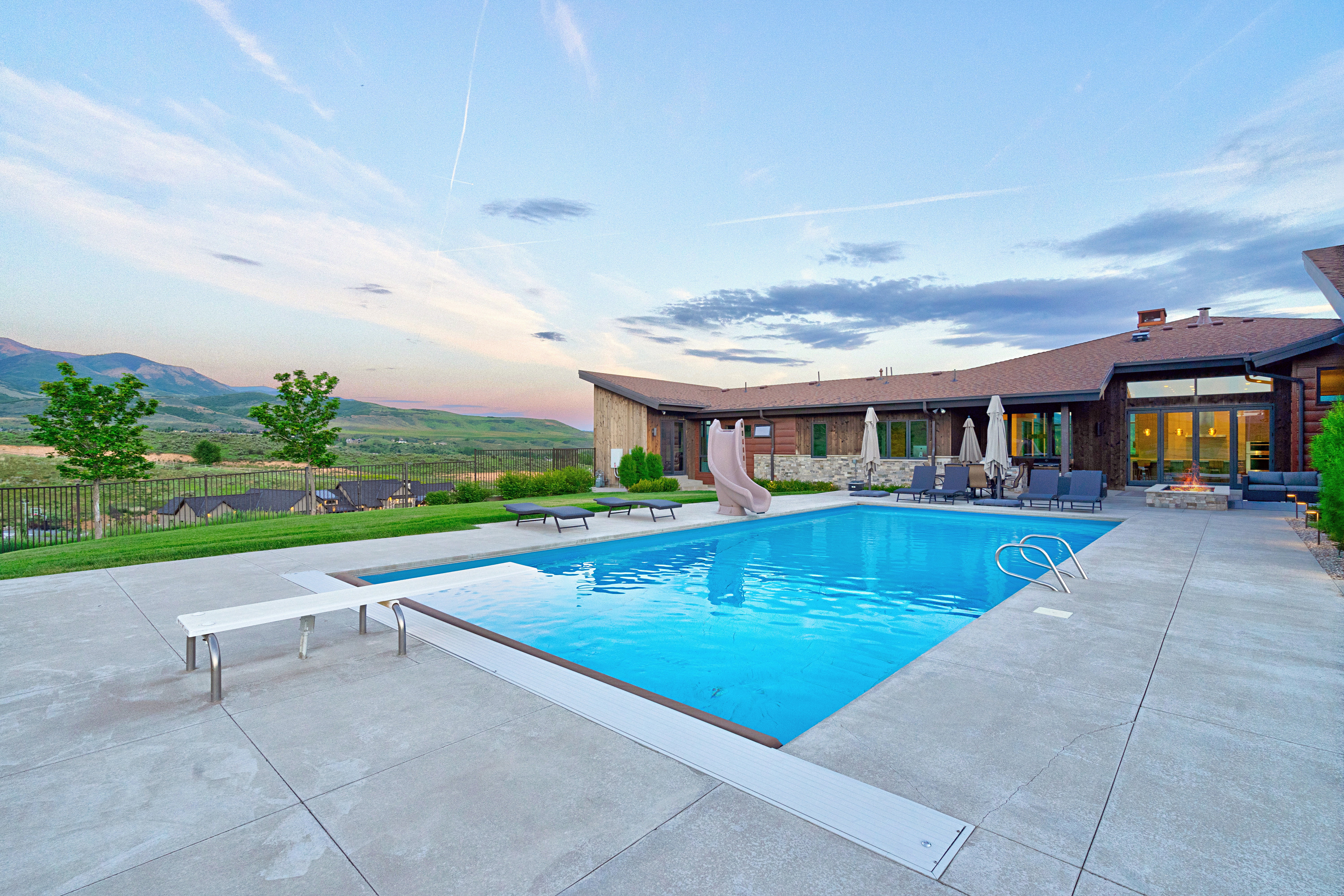 Outdoor swimming pool with a diving board and attached slide, surrounded by a concrete patio