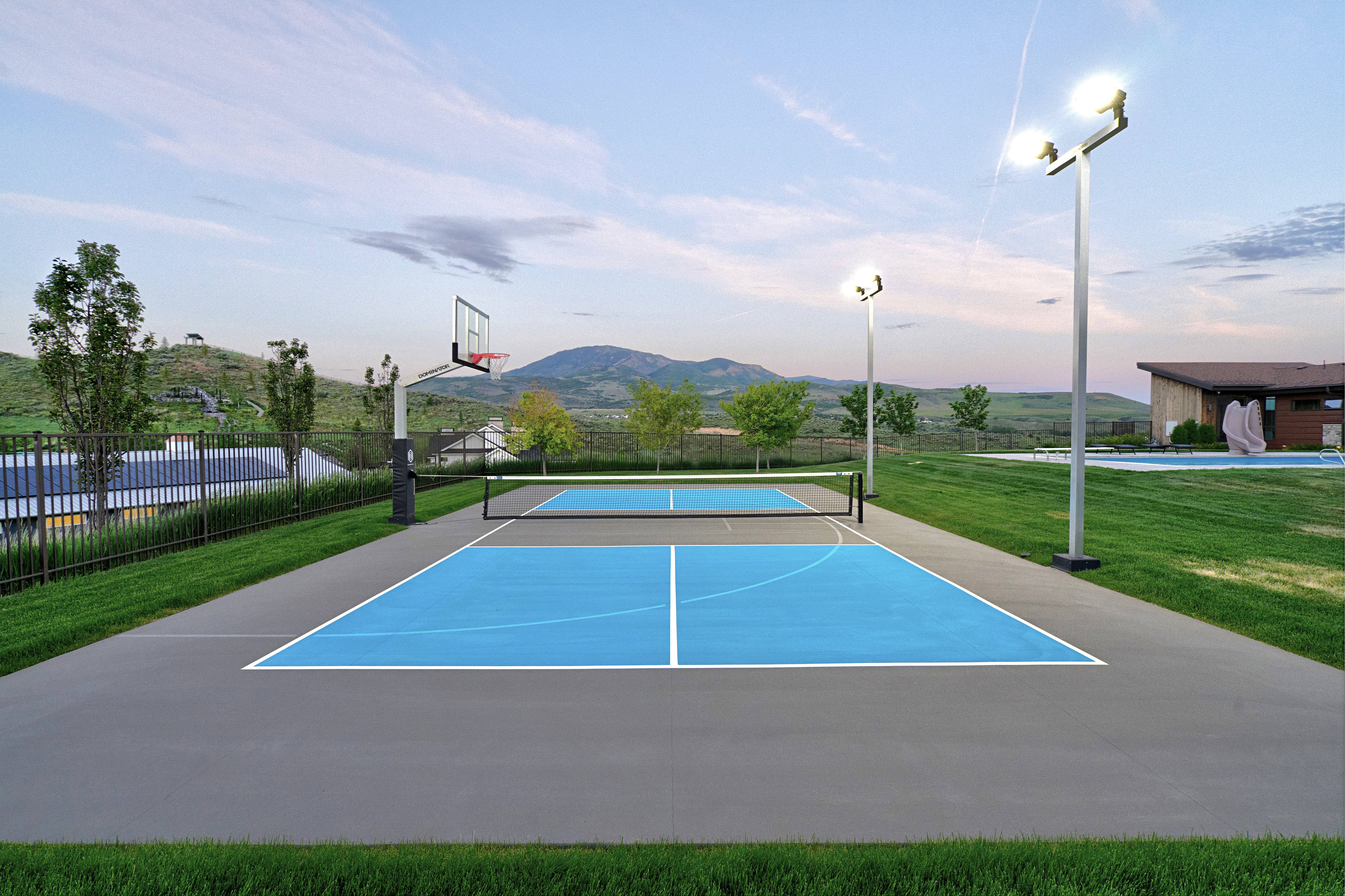 Multi-sport court featuring a basketball hoop, pickleball markings, and two tall athletic light poles