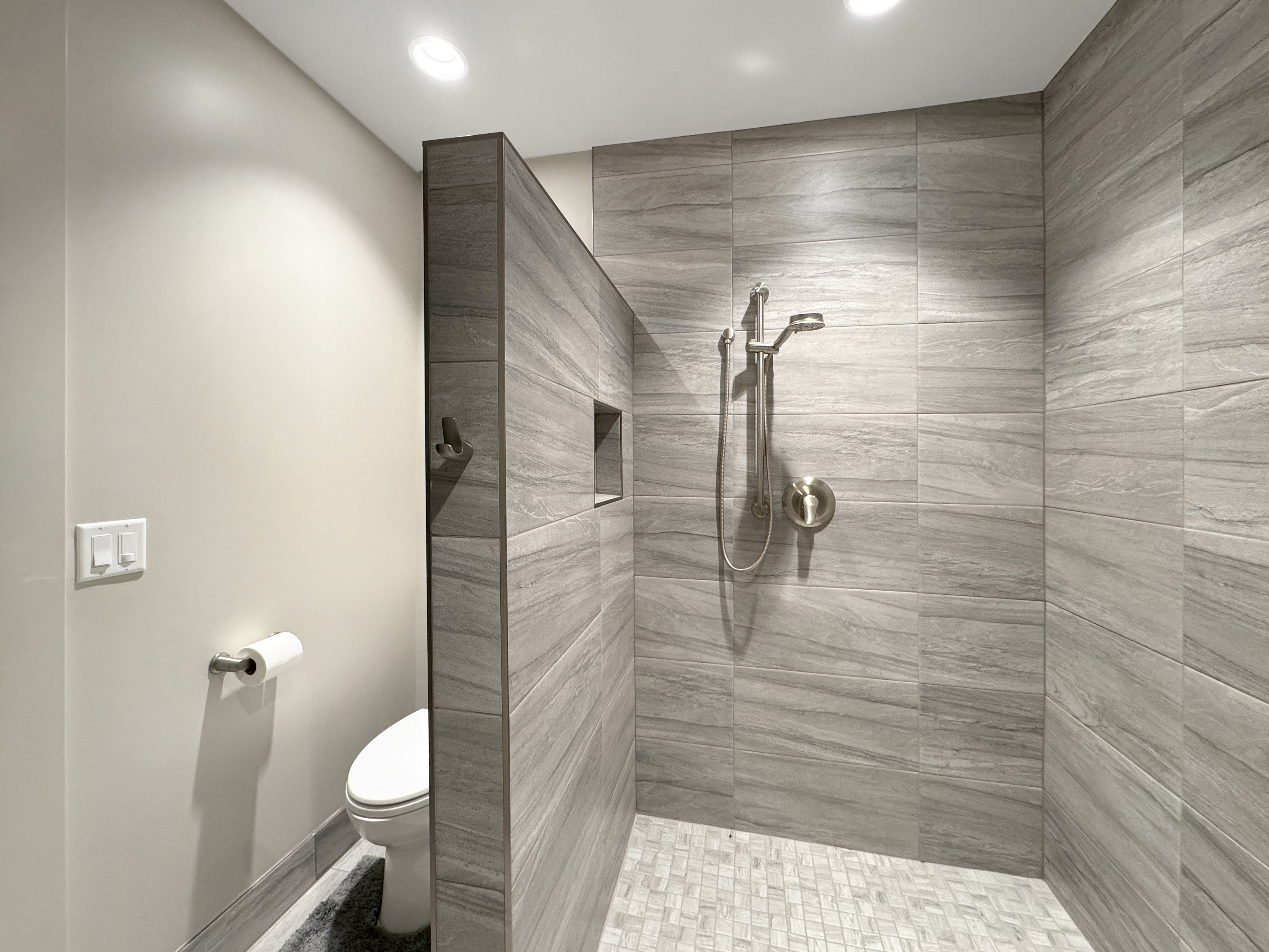 Walk-in shower featuring large format gray tile walls with a recessed niche and a brushed nickel shower system