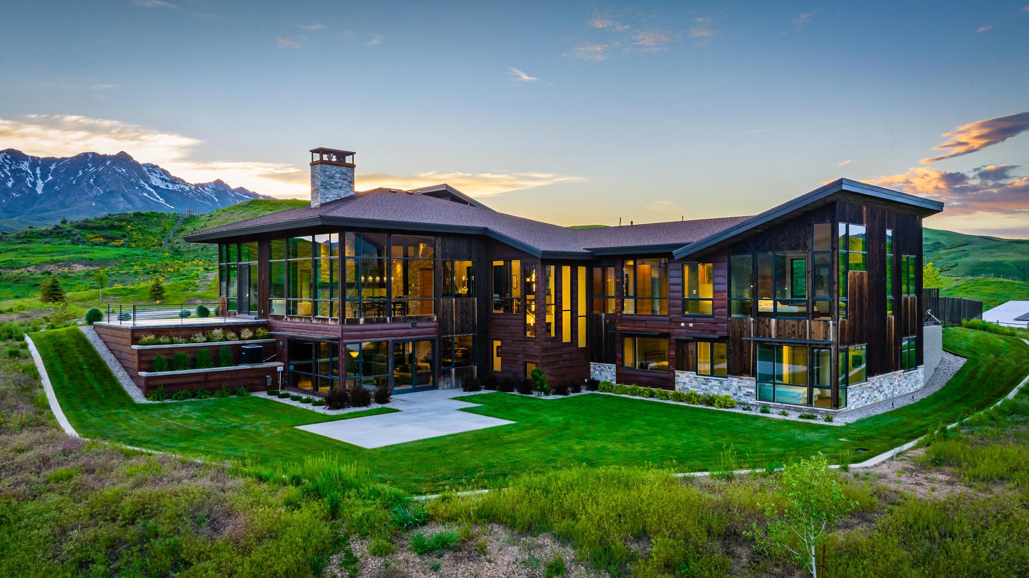 Modern architectural residence featuring extensive glass facades, a stone chimney, a multi-level wood exterior, and a flat roofline