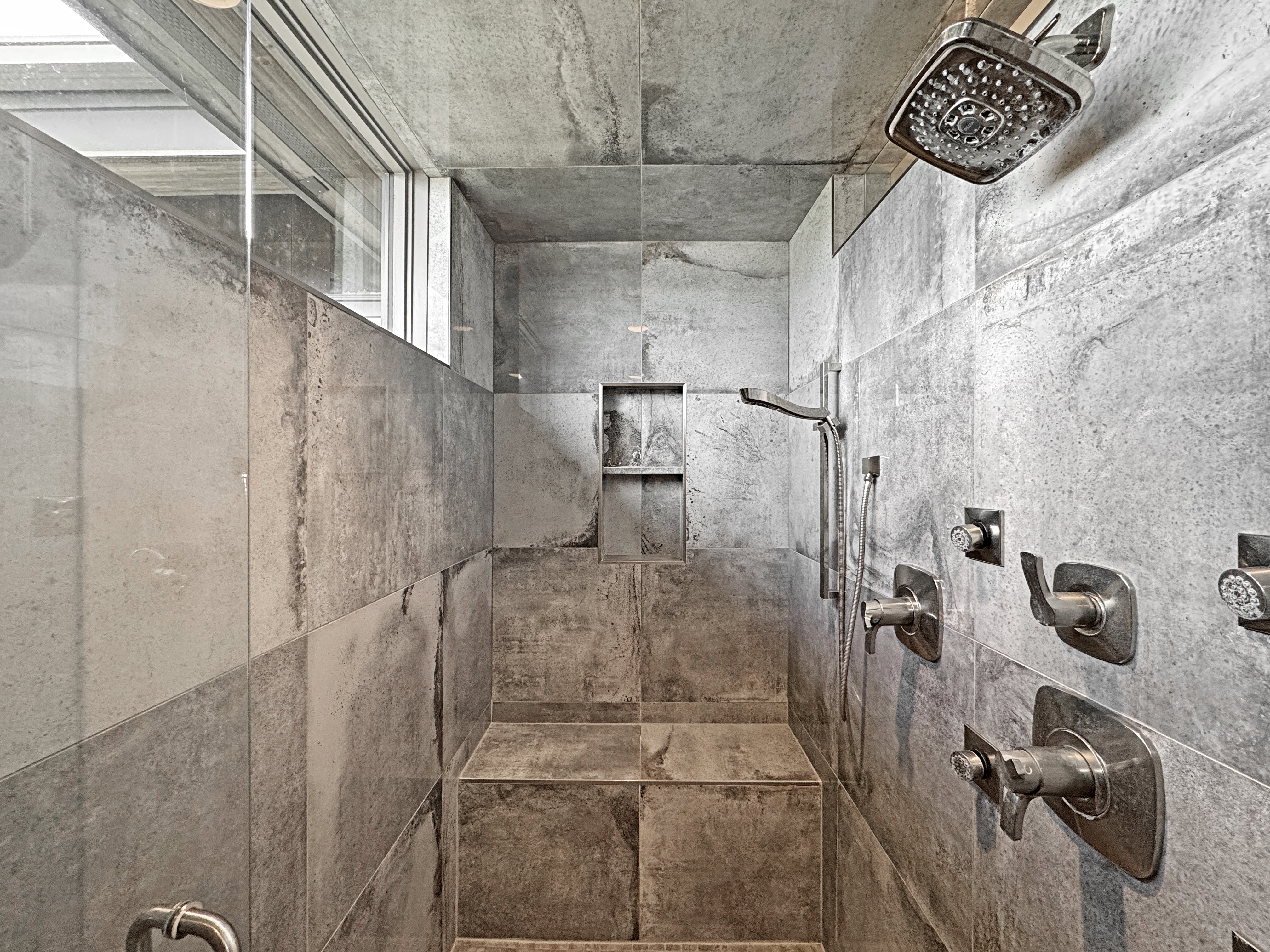 Shower with full tile surround, integrated bench seating, built-in shelving, and multiple showerheads